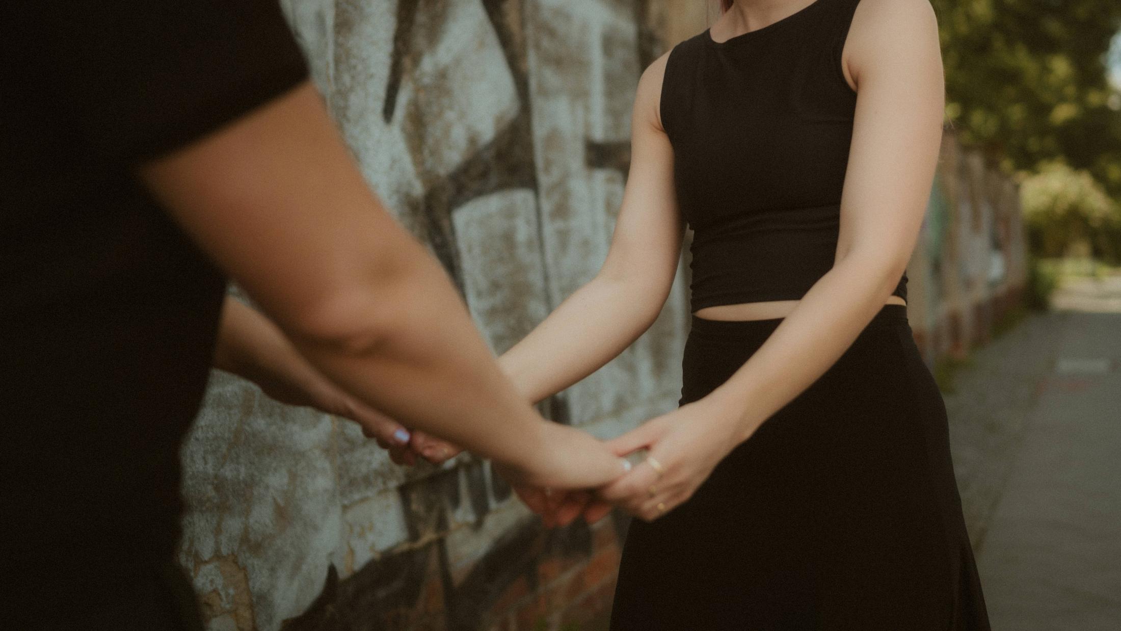 Noah and Michèle holding hands on the pavement beneath the graffiti wall.