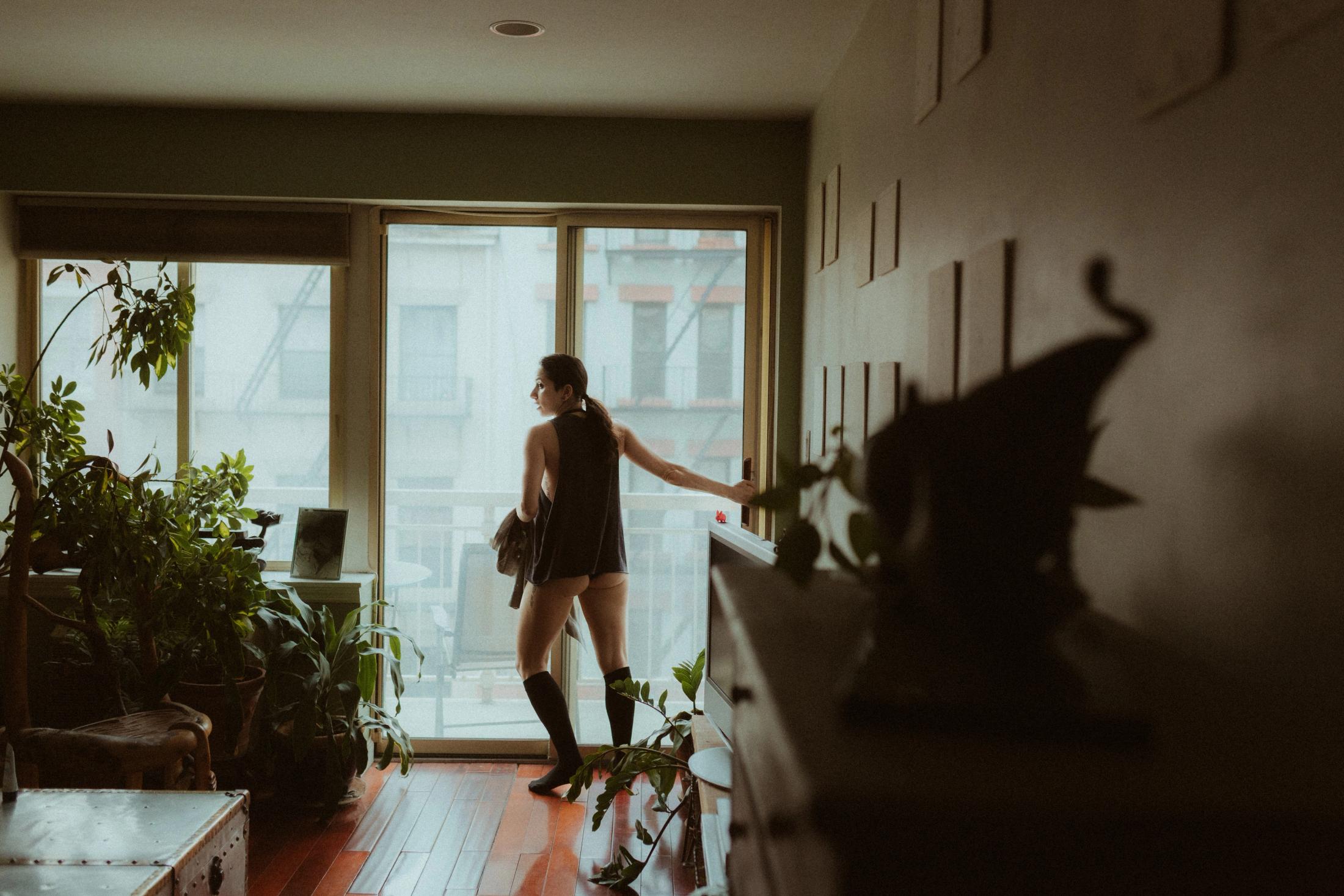 Maya silhouetted at the open balcony door among houseplants.