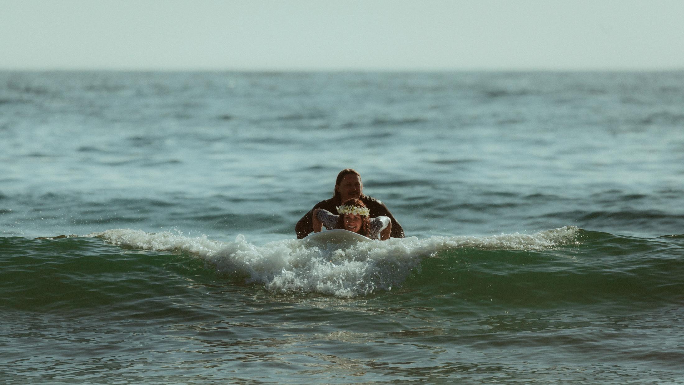 A breaking wave rising in front of Petra and Roman on their board