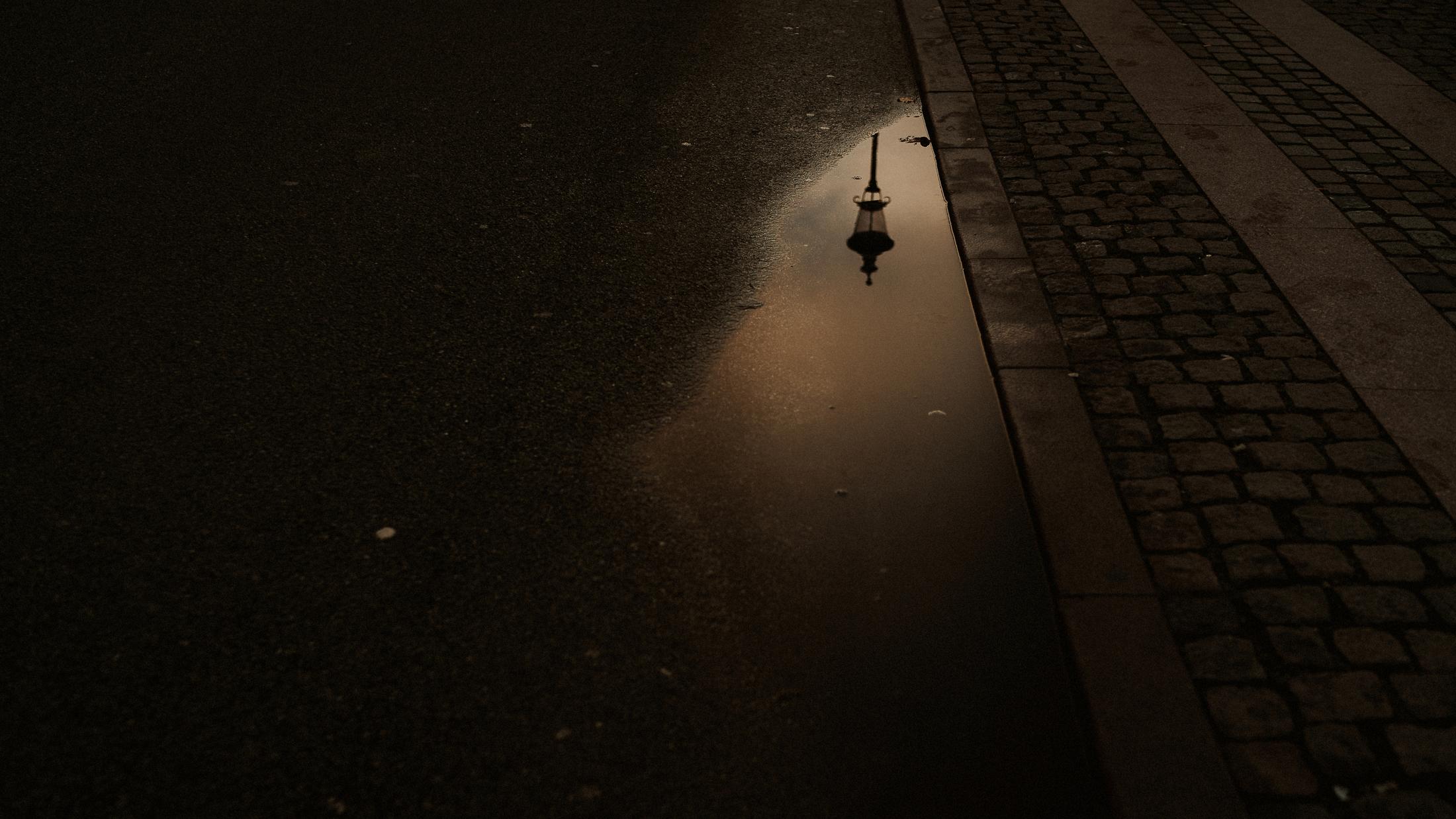 A street lamp is reflected in a puddle beside a cobbled pavement.