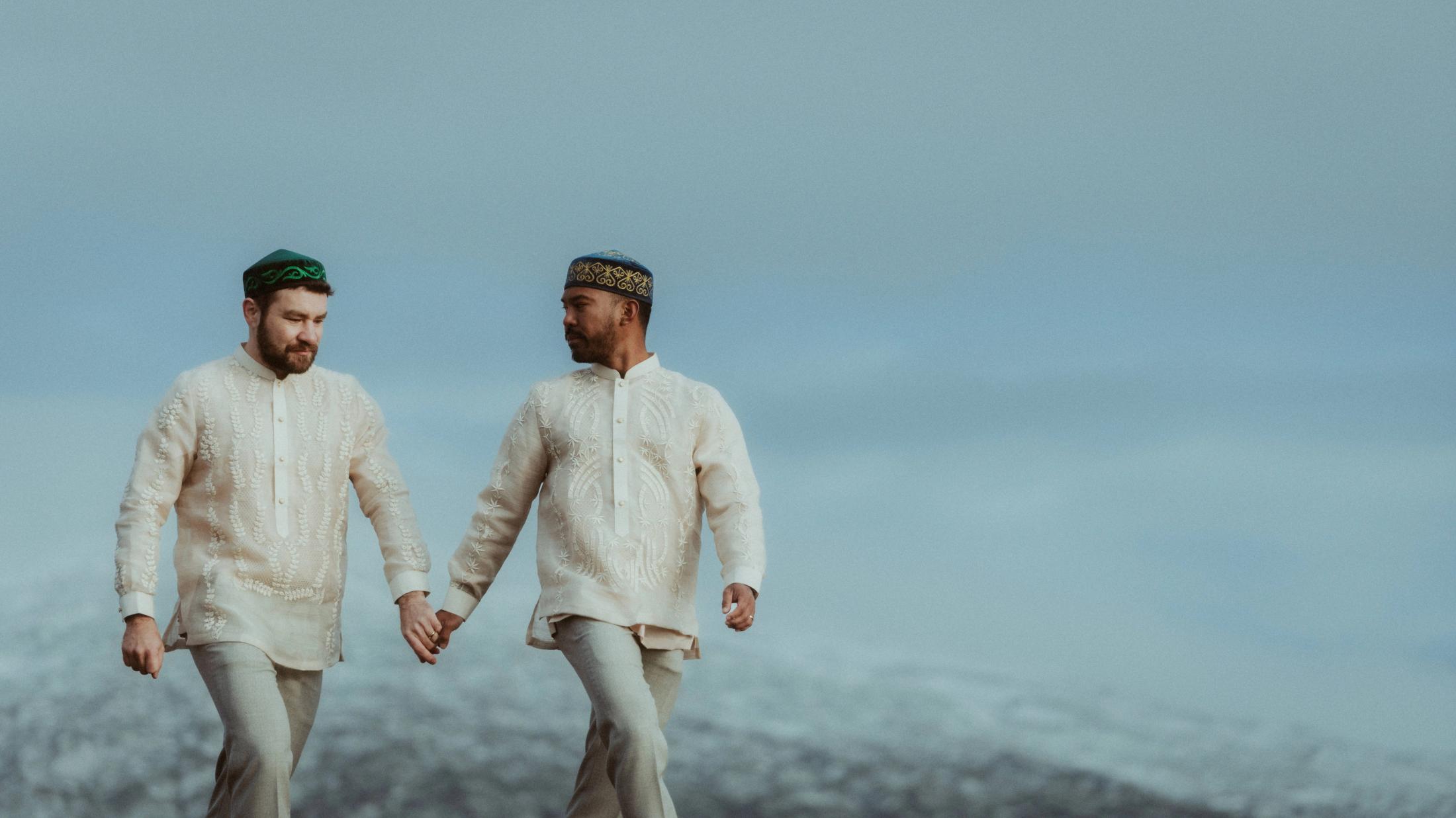 Kris und Ilya gehen Hand in Hand unter einem hellen blaugrauen Himmel.