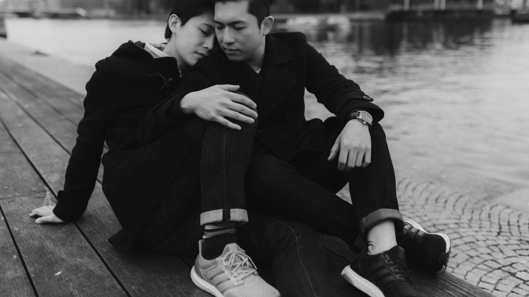 Kevin and Terence sit close together beside the water.