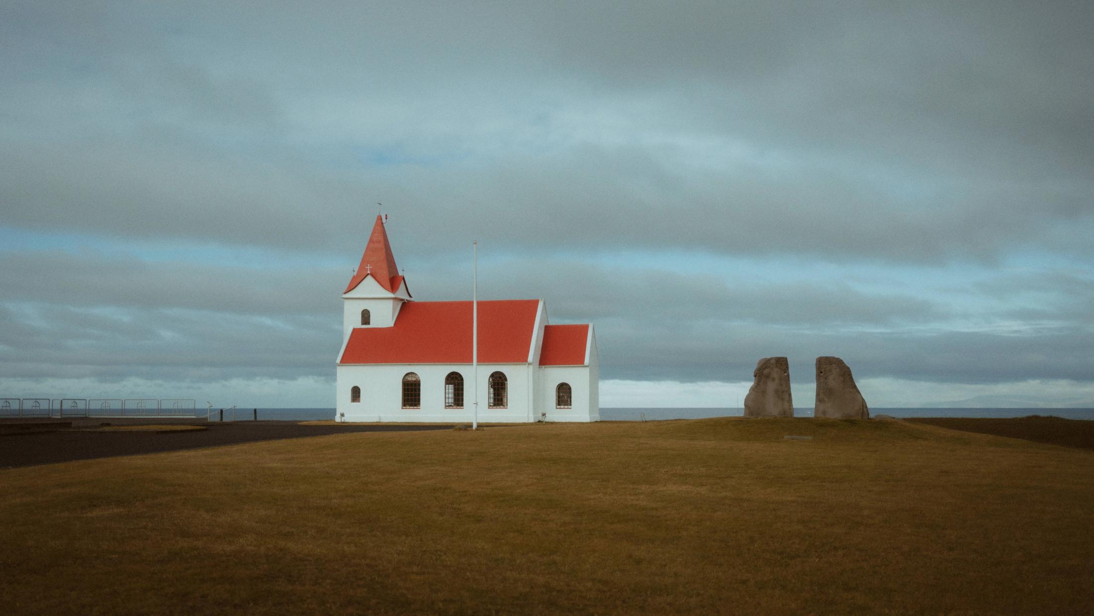 Eine kleine weiße Kirche mit rotem Dach steht allein unter grauen Wolken.