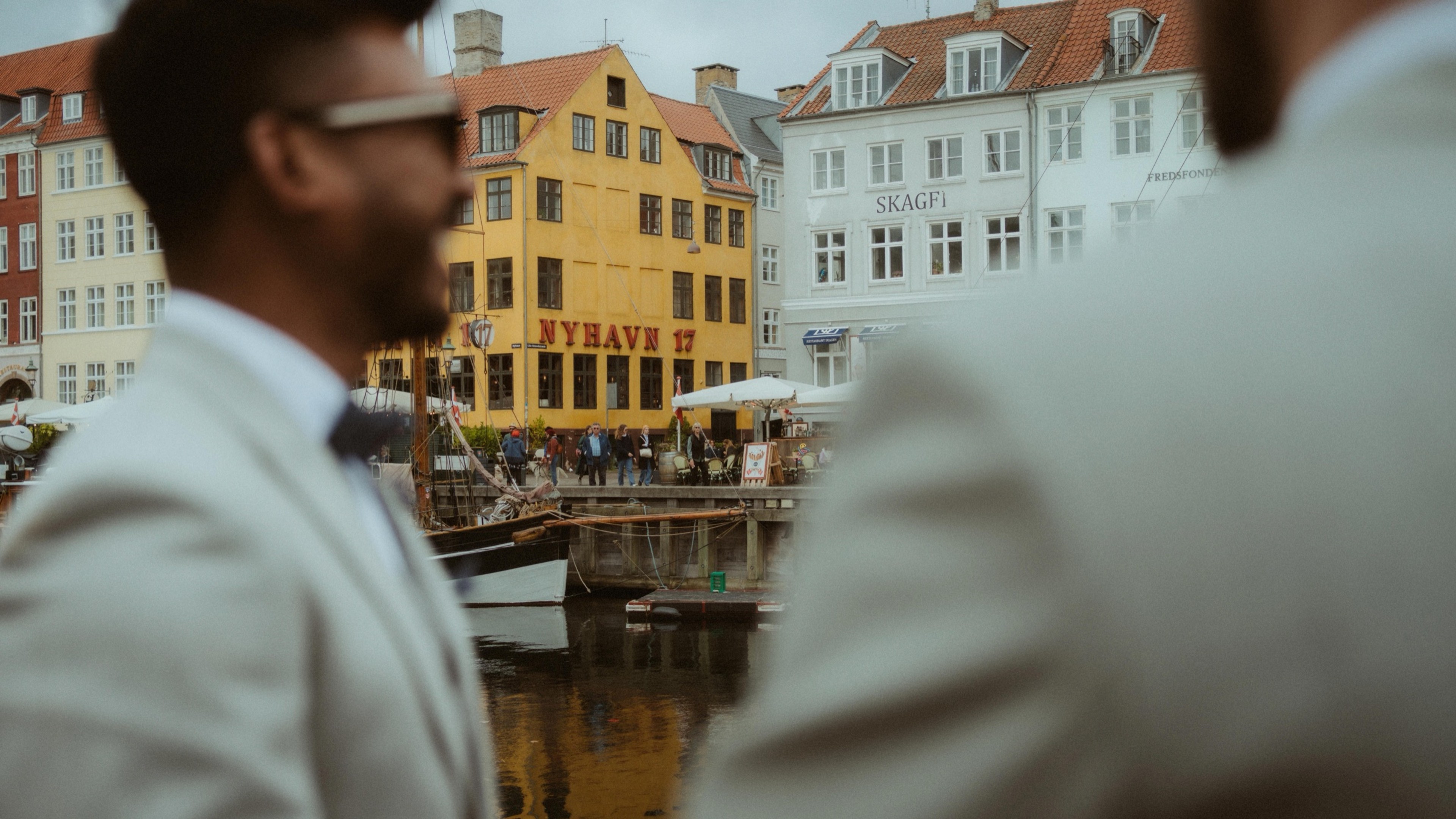 Blurred couple in the foreground with the colourful Nyhavn 17 facade and canal water in focus behind them in Copenhagen