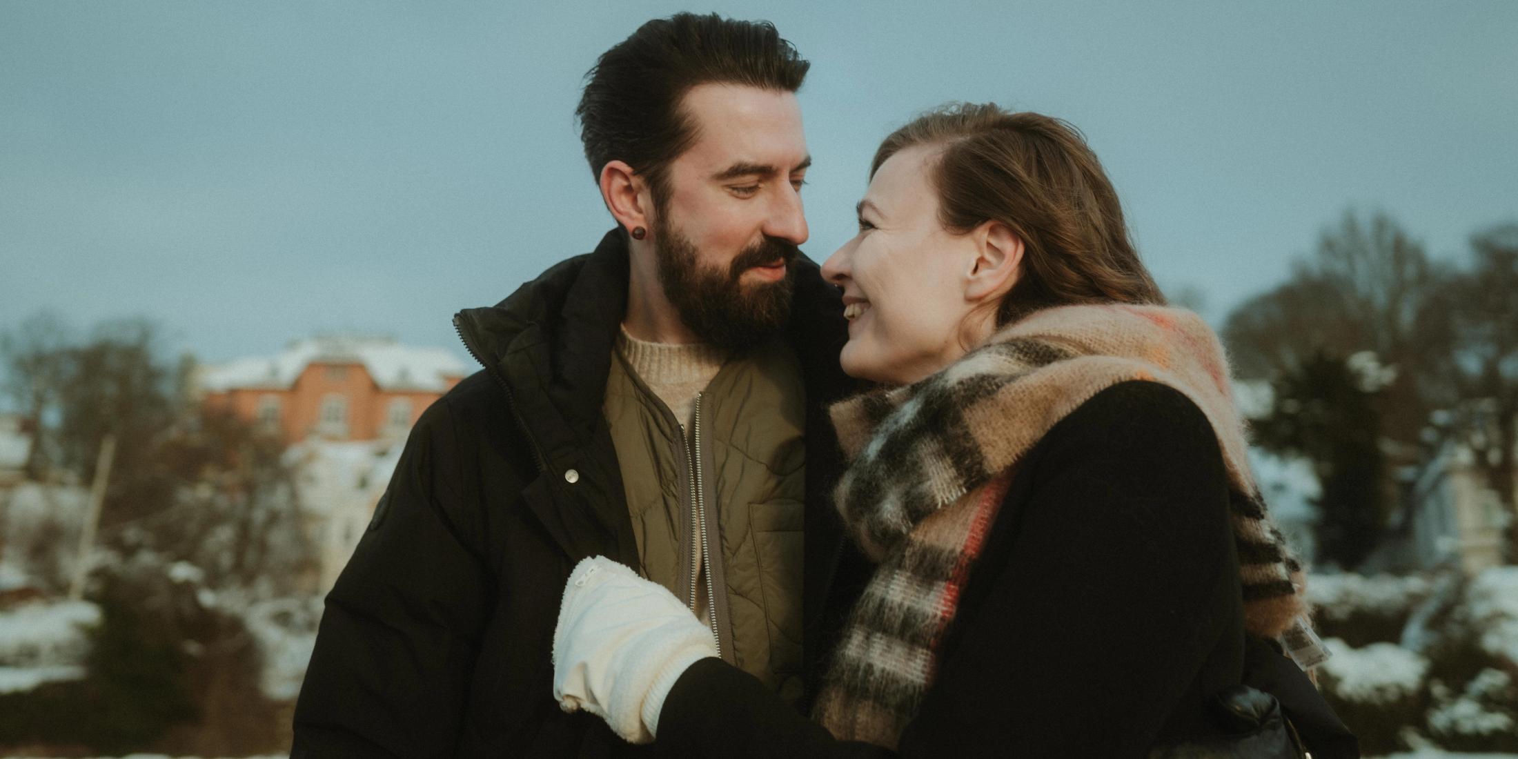 Mieke and Tim stand close together in winter and smile at each other.