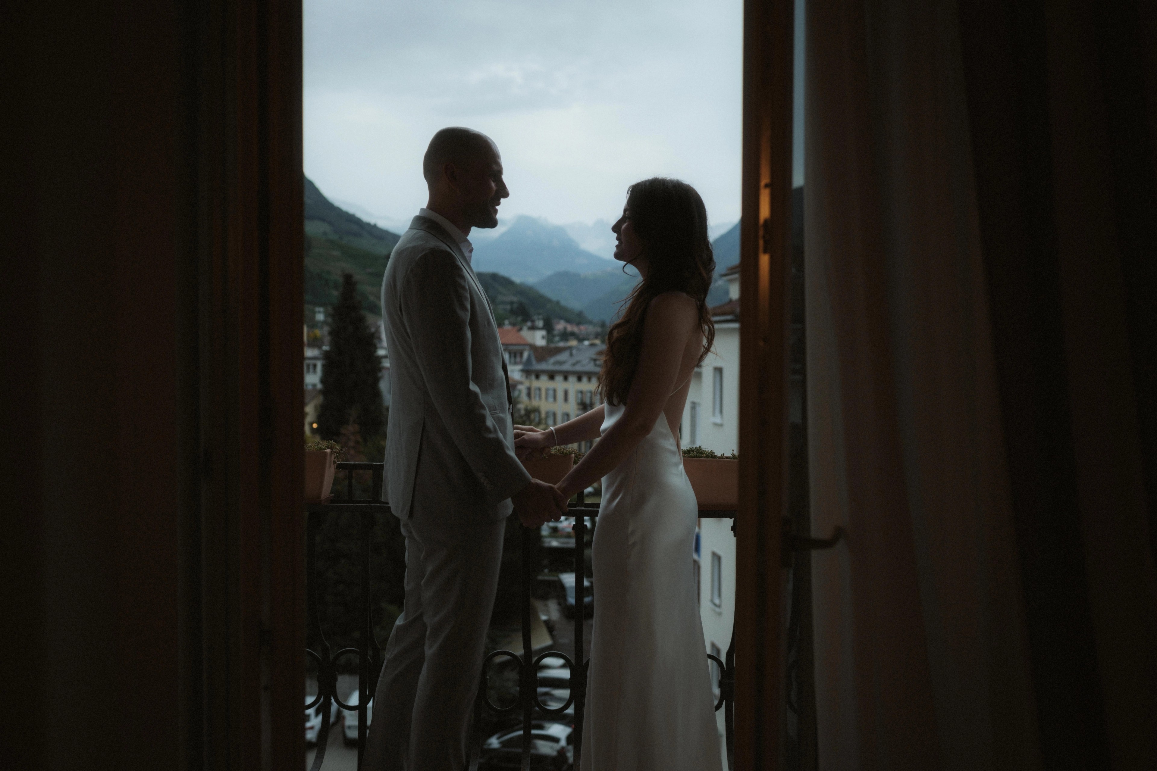 Jana and Steffen stand in silhouette beside a bright hotel window.