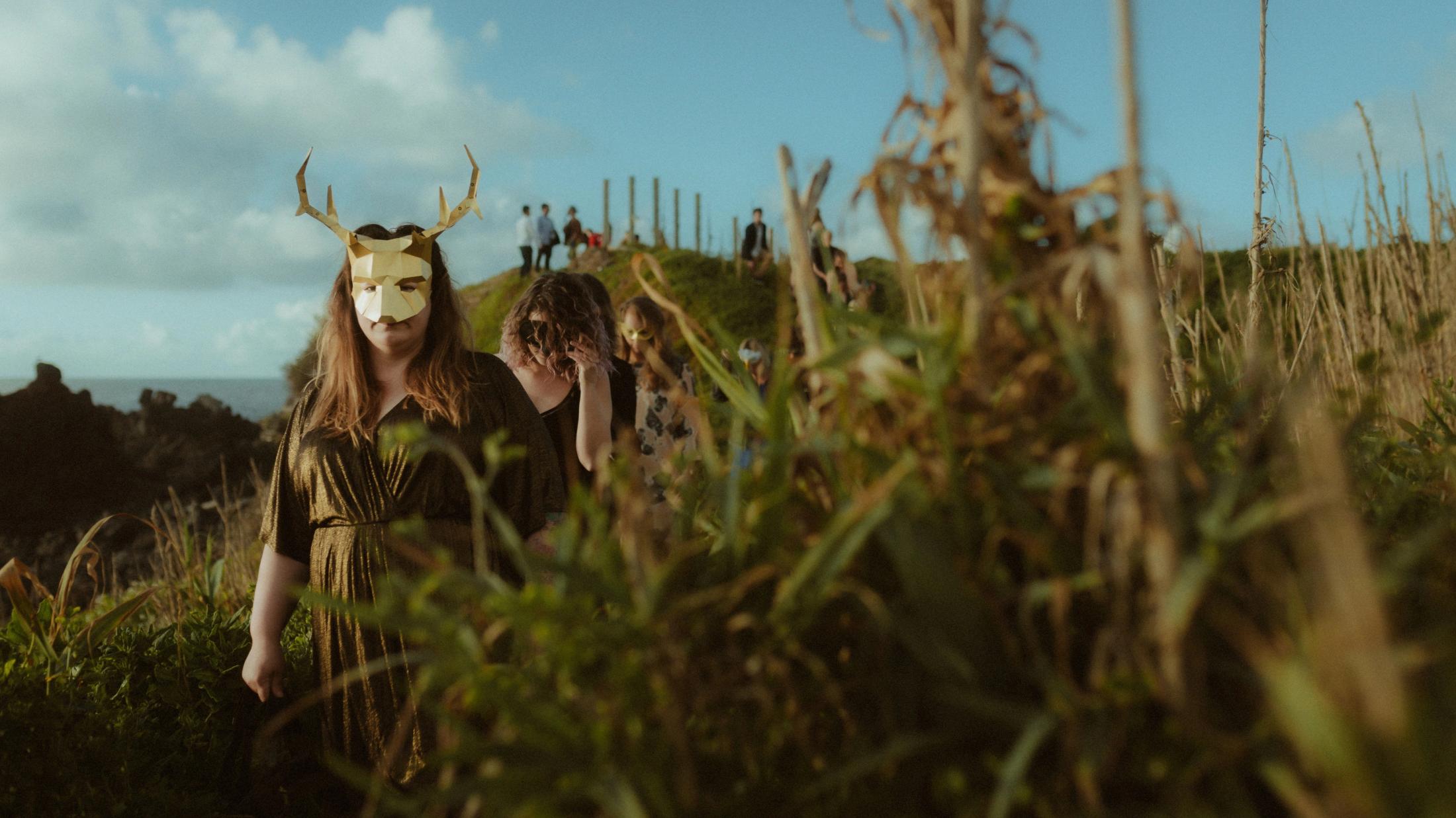 A participant in an animal mask leads others toward the beach.