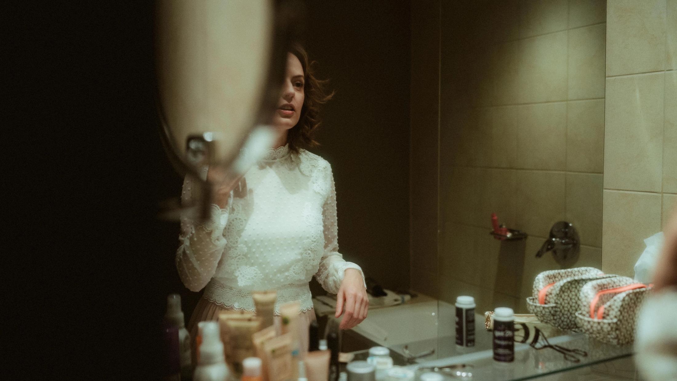 Ari getting ready in a cluttered bathroom mirror