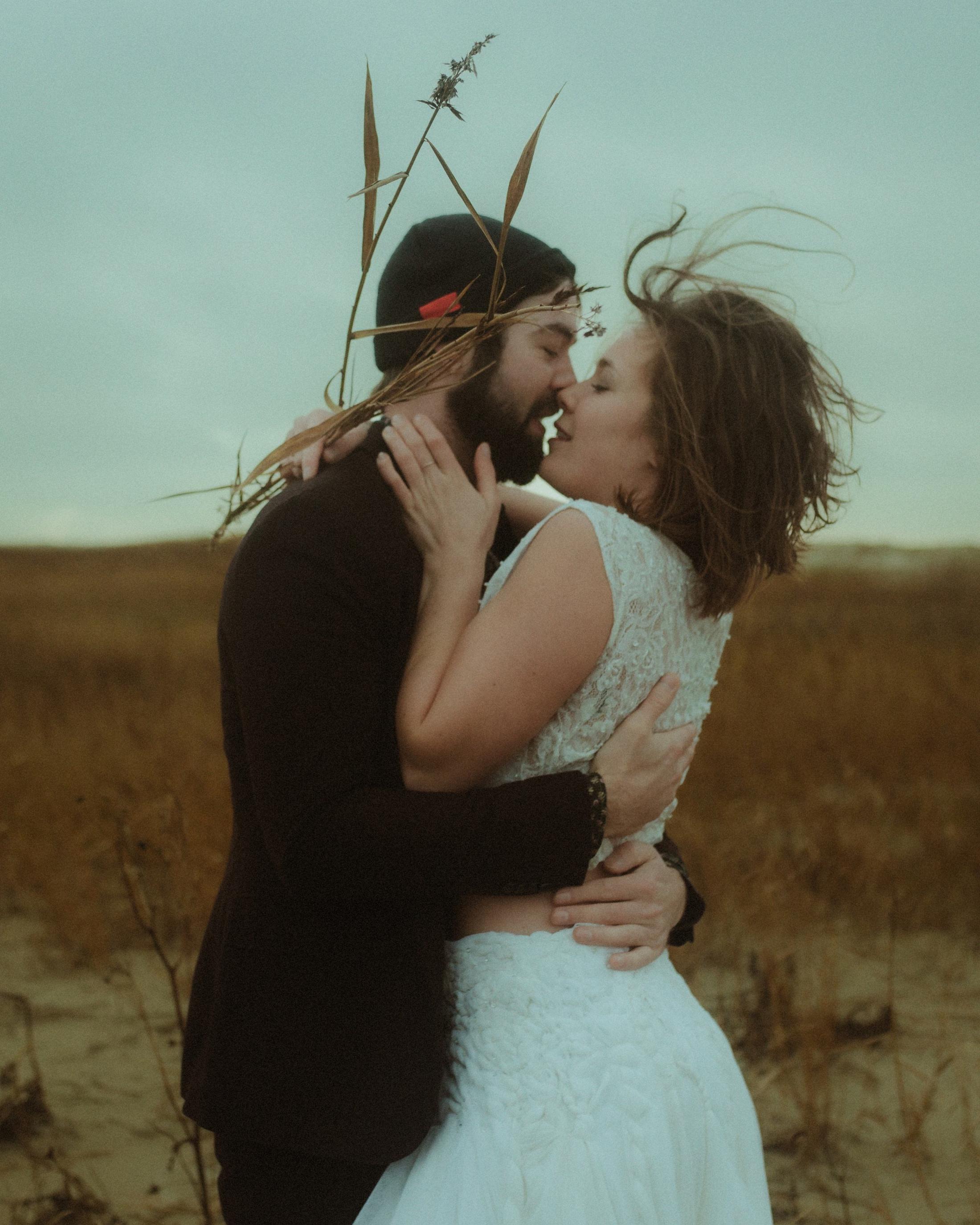 Vertical portrait of Anni and Daniel kissing with reeds between them.