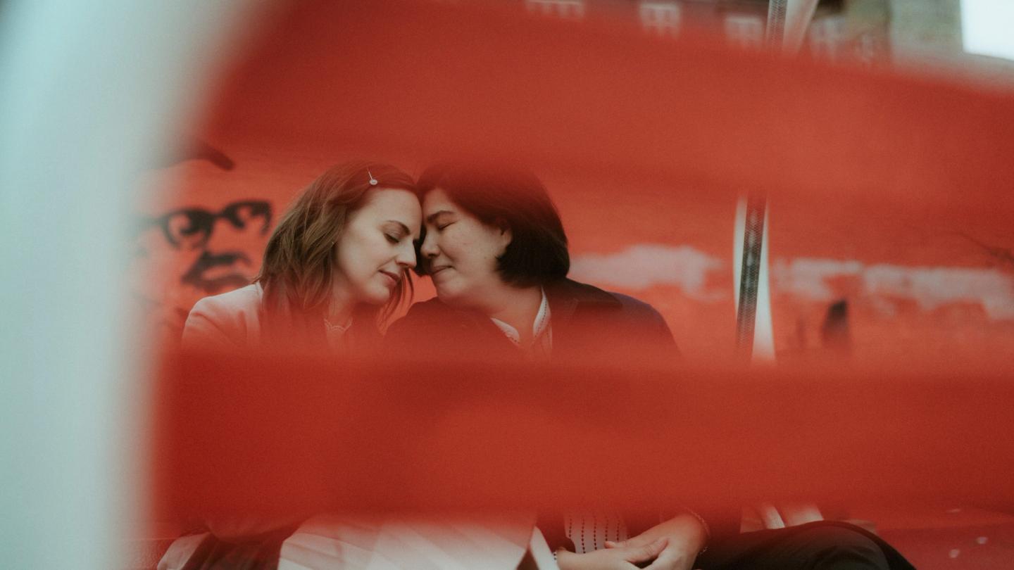Ari and Pia are photographed through the red back of a bench.