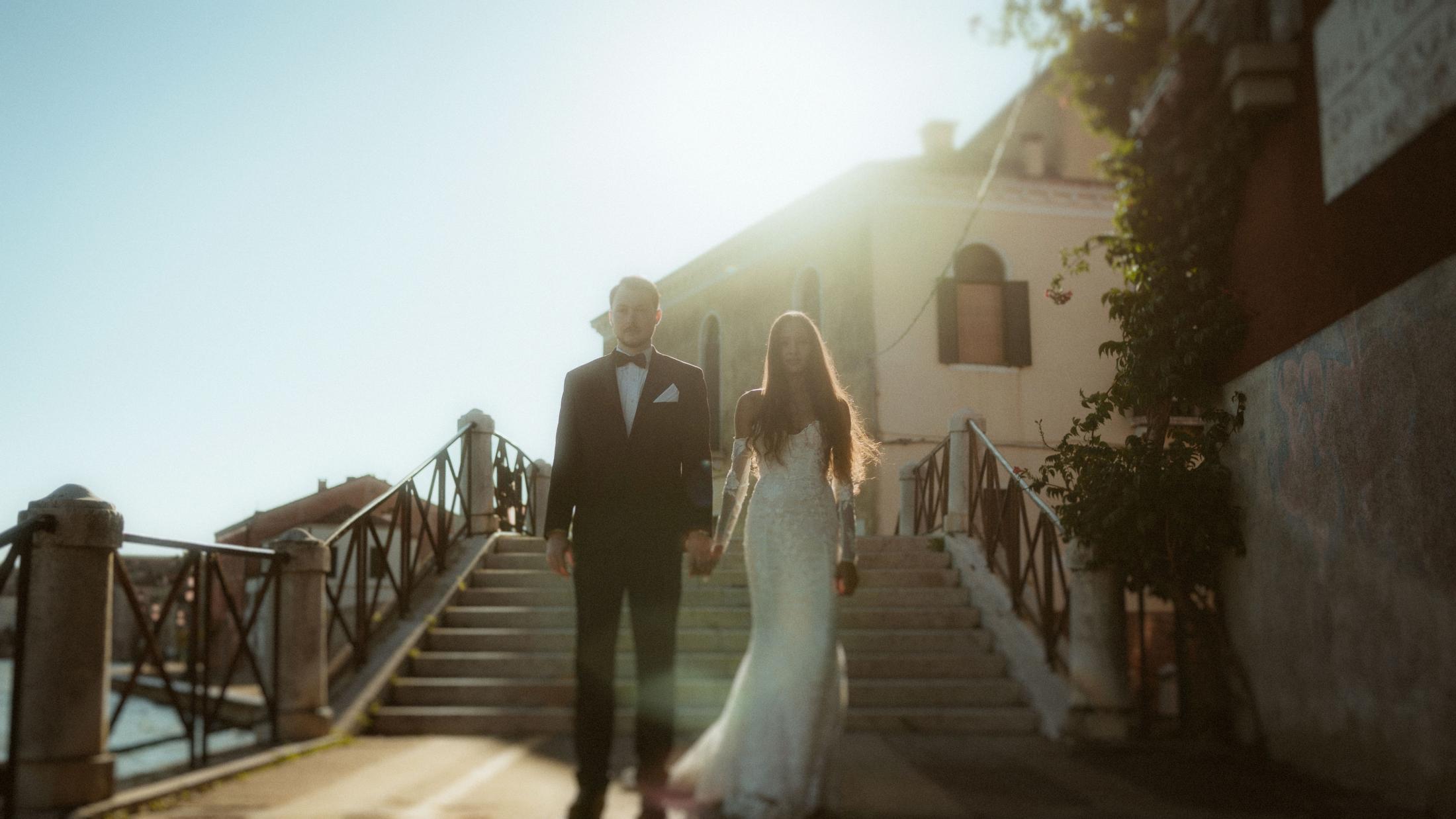 The couple walks up outdoor steps through strong evening backlight.