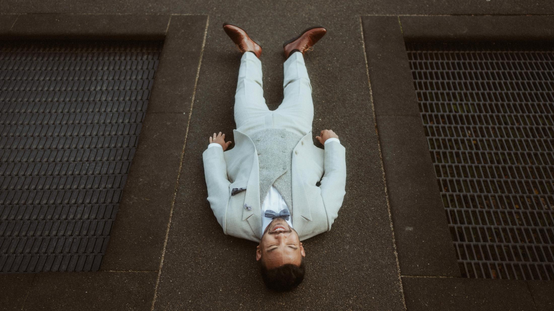 Kris lies flat on the pavement in his light suit.