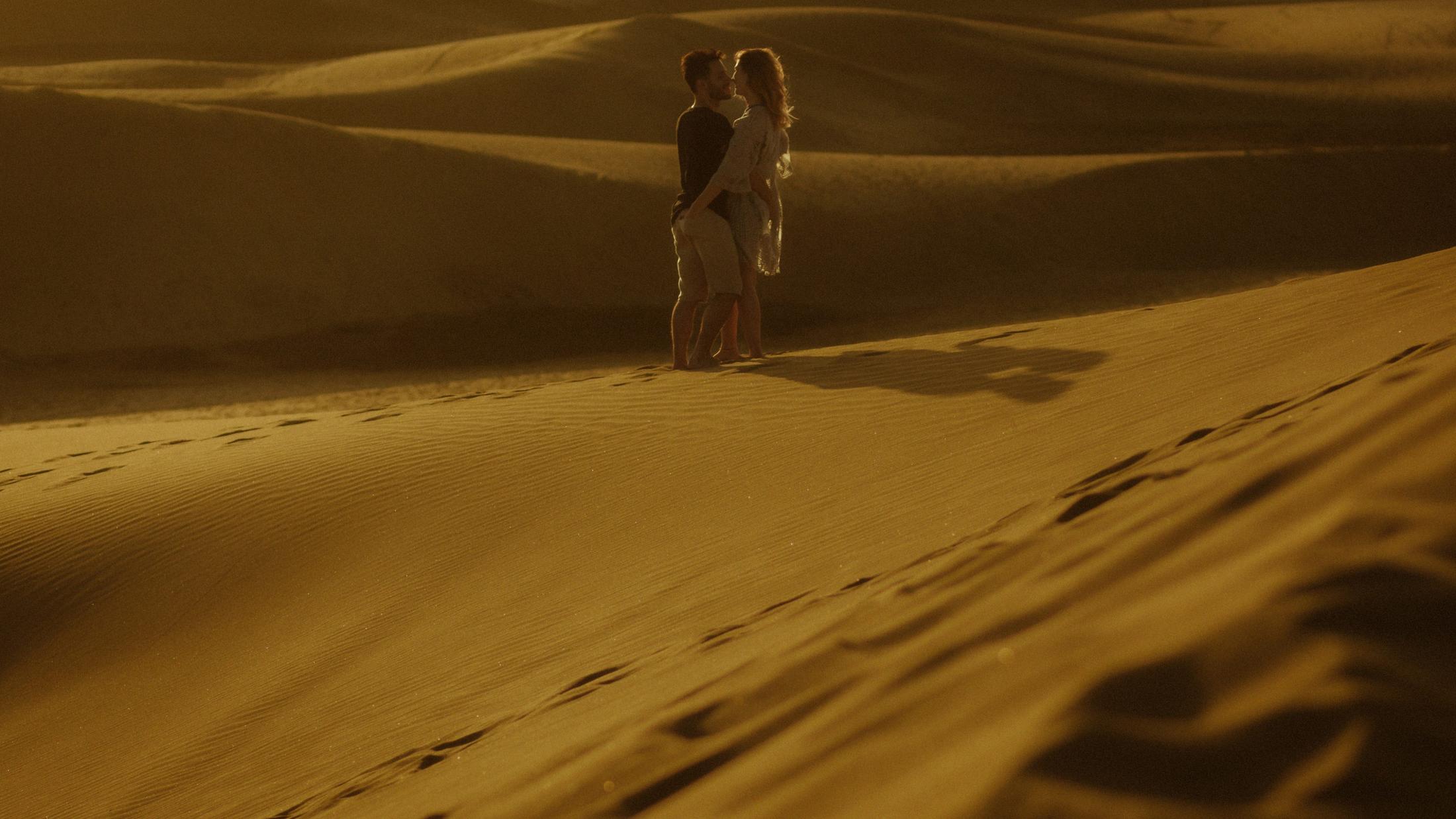 Katja and David embracing as small figures on a bright sand slope.