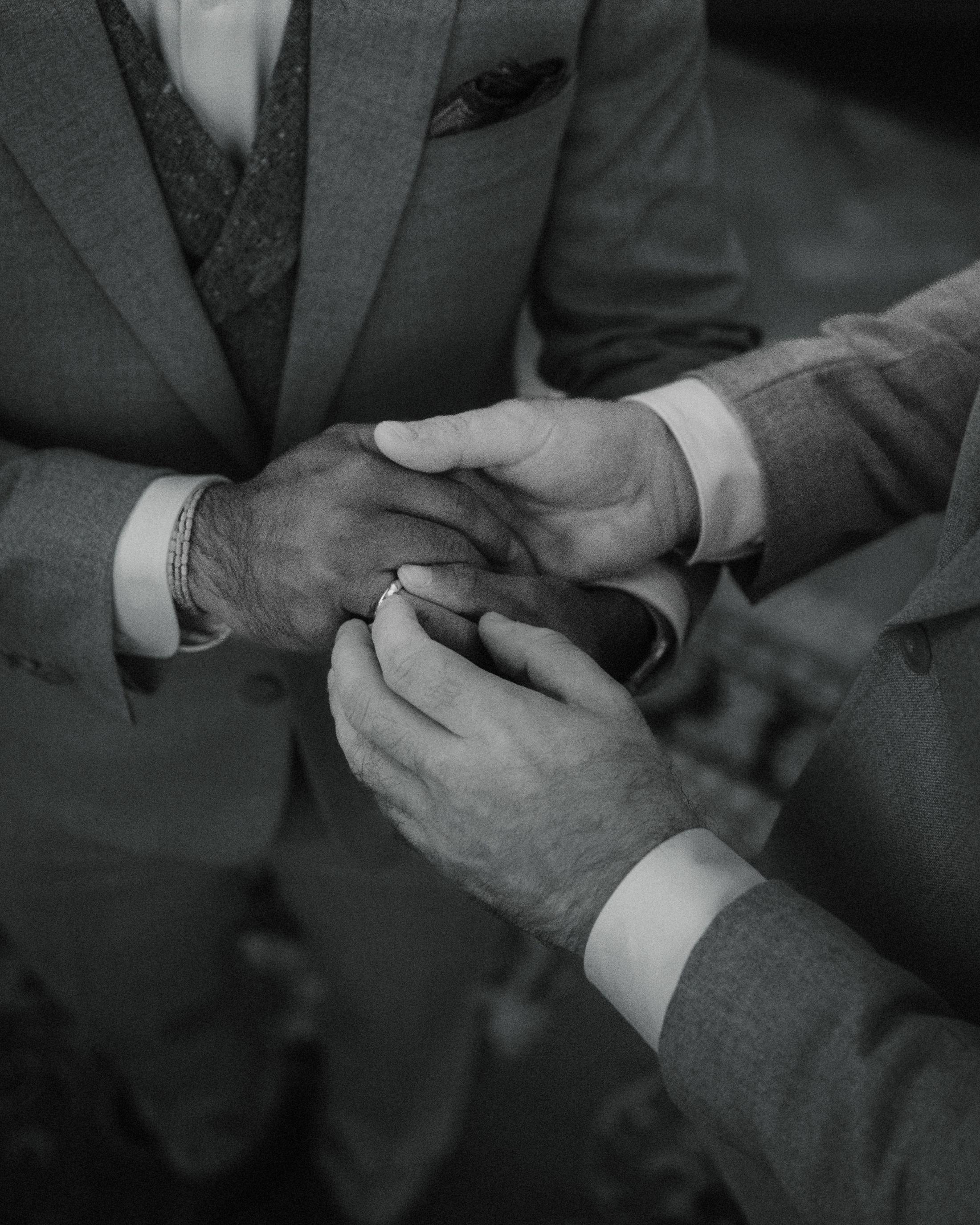 Black-and-white close-up of a wedding ring being placed on a finger.