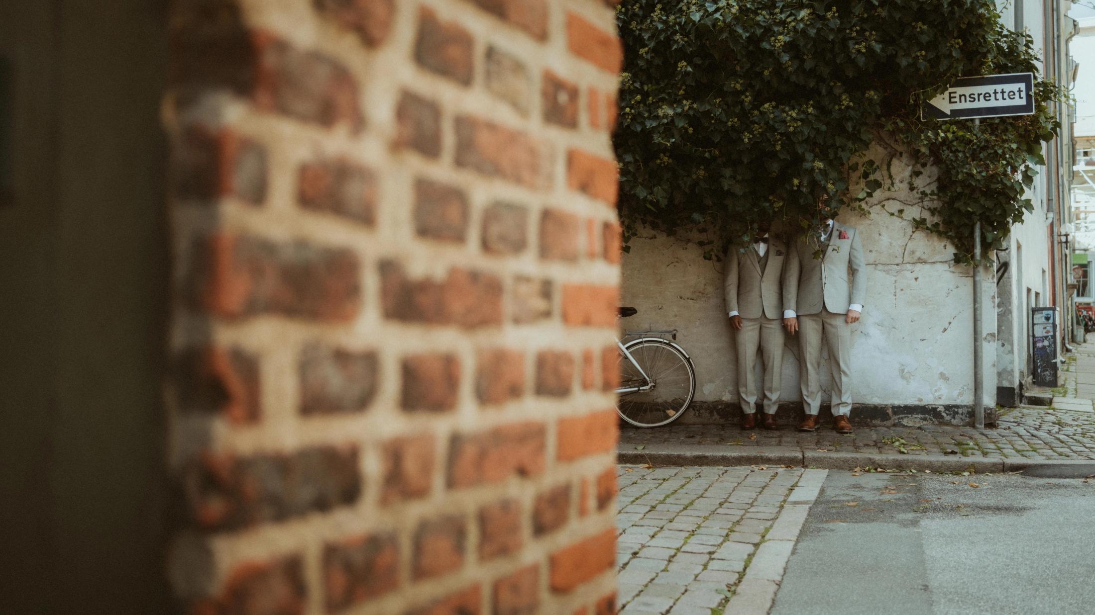 Kris and Ilya stand almost hidden beside a brick wall and dense green ivy.