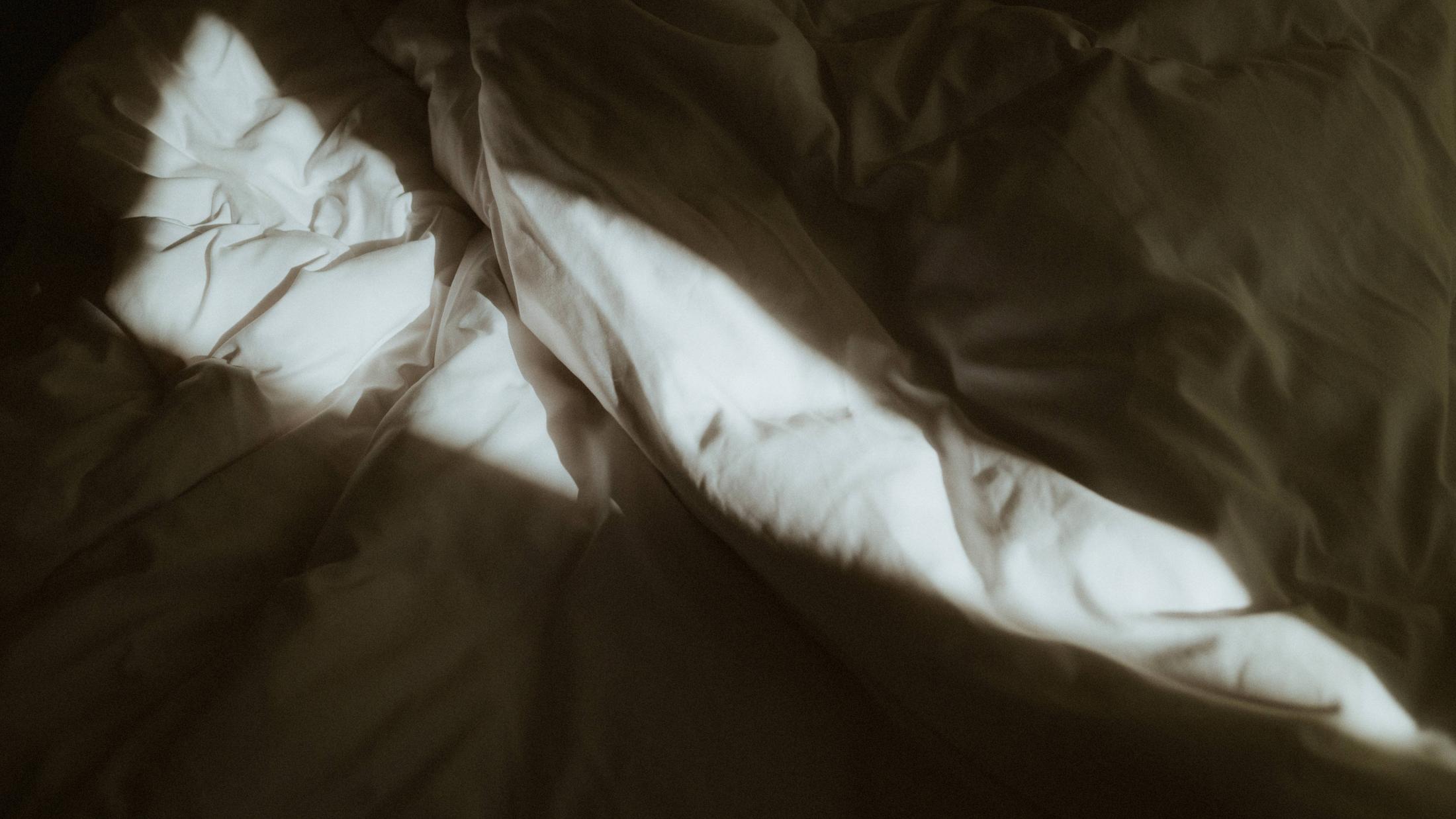 White bed sheets crossed by a bright strip of window light.