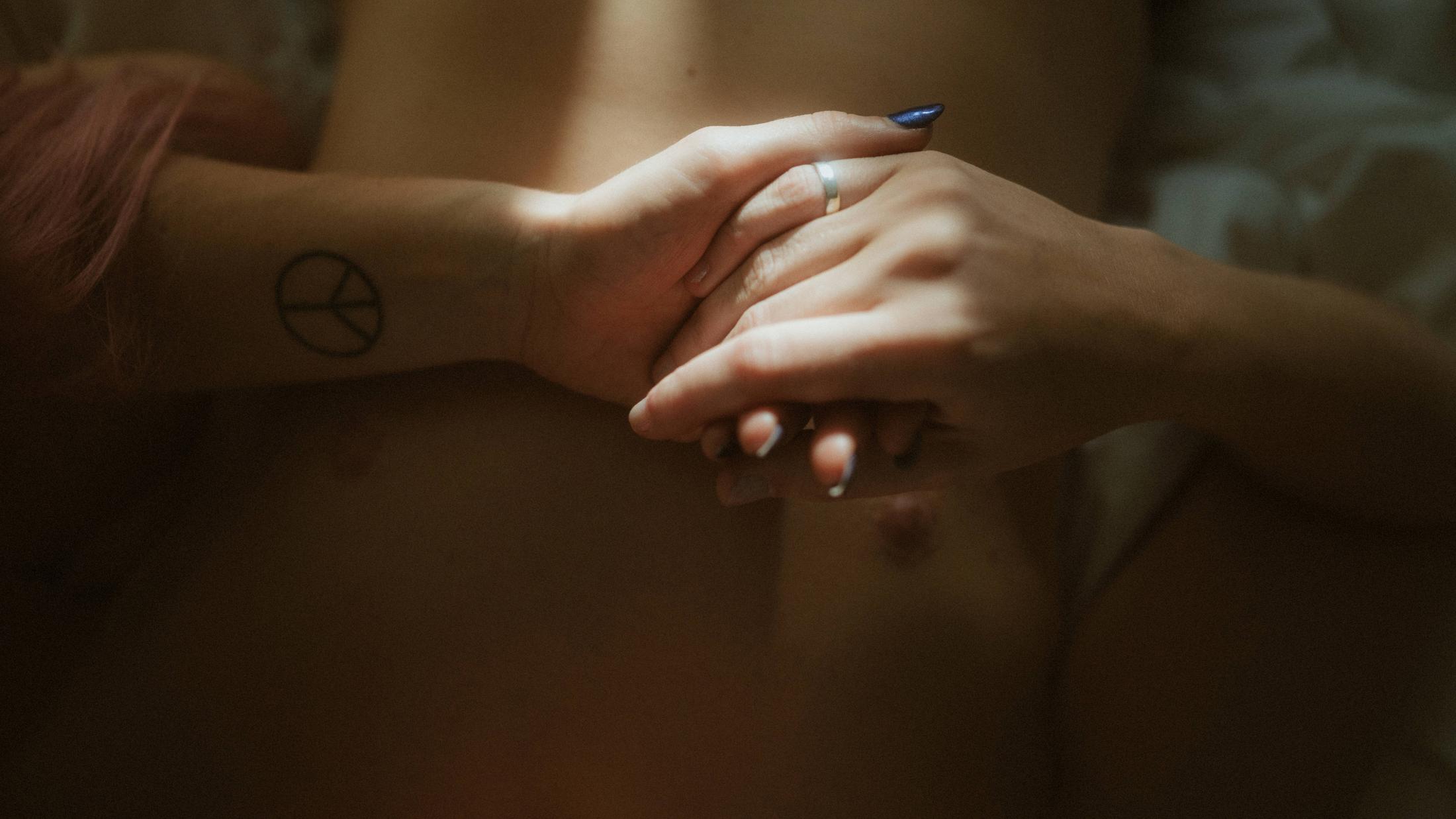 Their hands joined over Noah's chest beside a small peace-symbol tattoo.