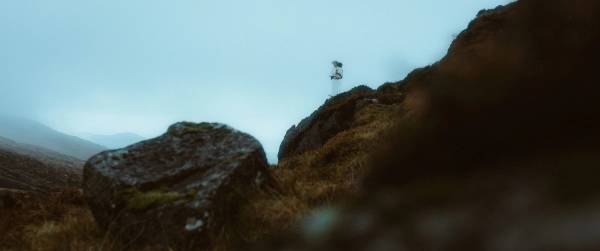 Two tiny figures stand on a rocky outcrop above a fog-filled valley in the Cooley Mountains.