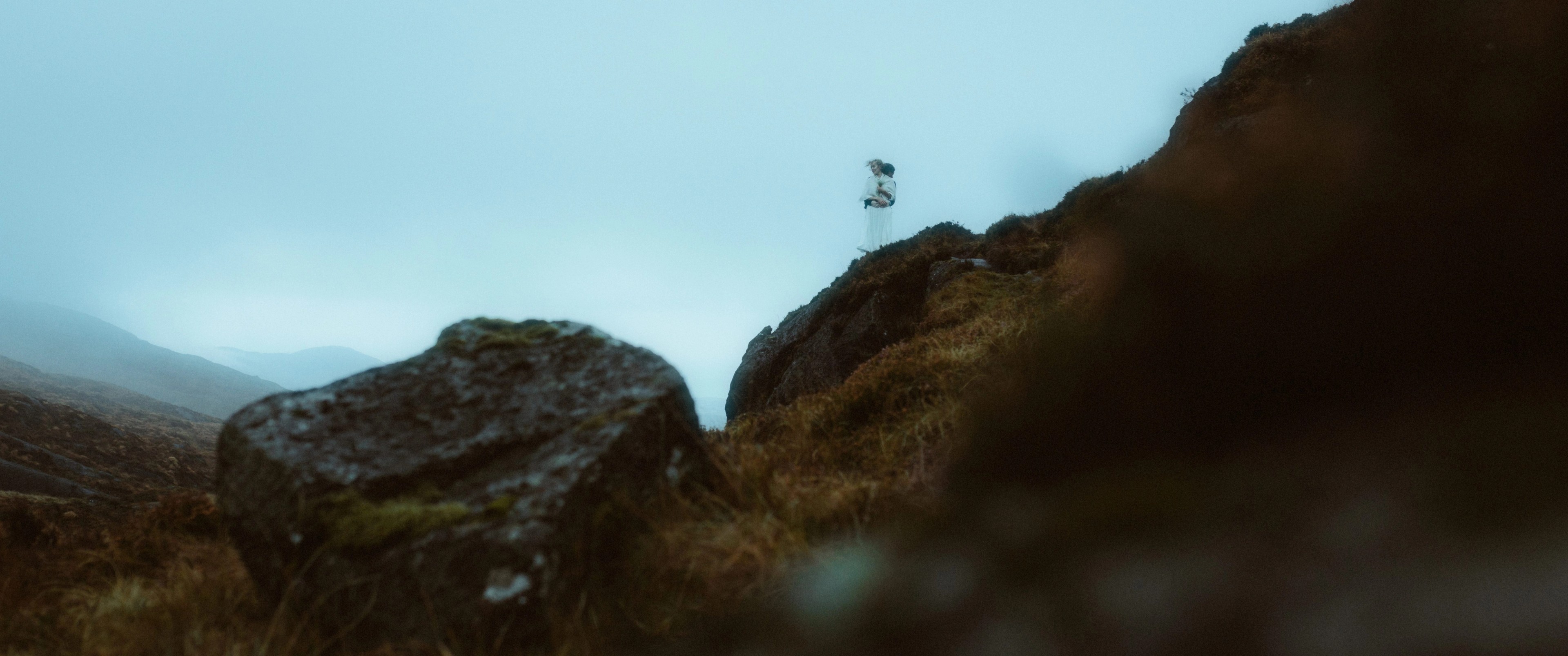 Zwei winzige Gestalten stehen auf einem Felsvorsprung über einem nebelgefüllten Tal in den Cooley Mountains.