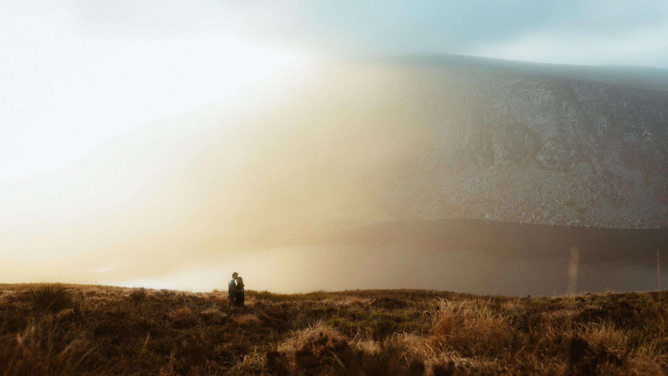Jule und Rory stehen klein in einer weiten Berglandschaft im tiefen Abendlicht.