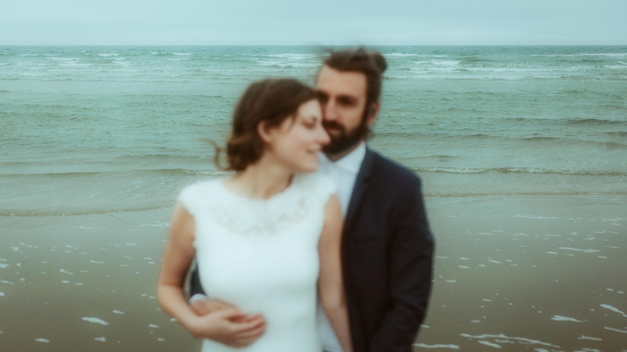 Bewusst unscharfes Porträt von Nina und Torben, die eng beieinander vor dem grauen Meer stehen.