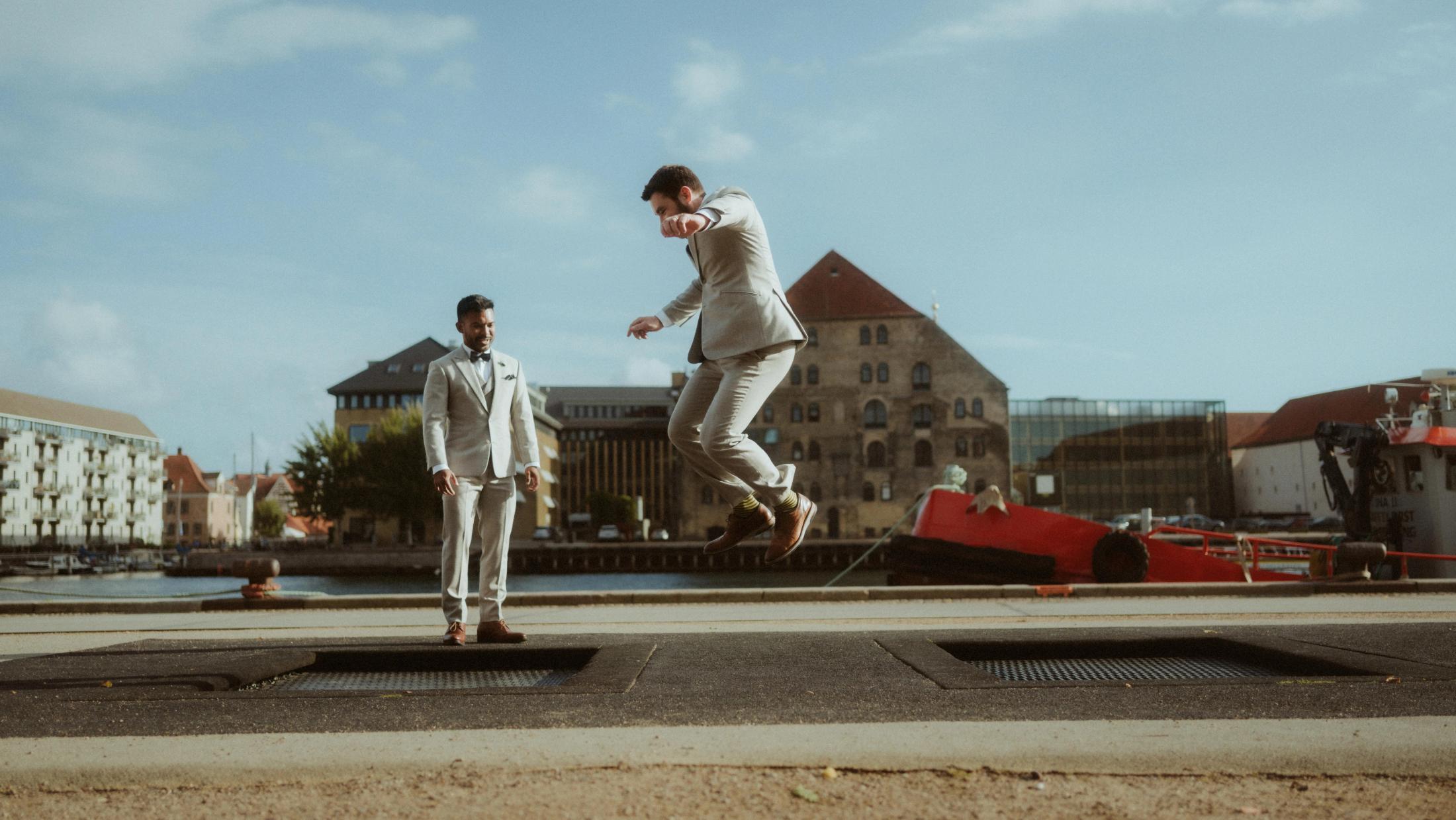 Ilya jumps into the air while Kris watches from across a Copenhagen plaza.