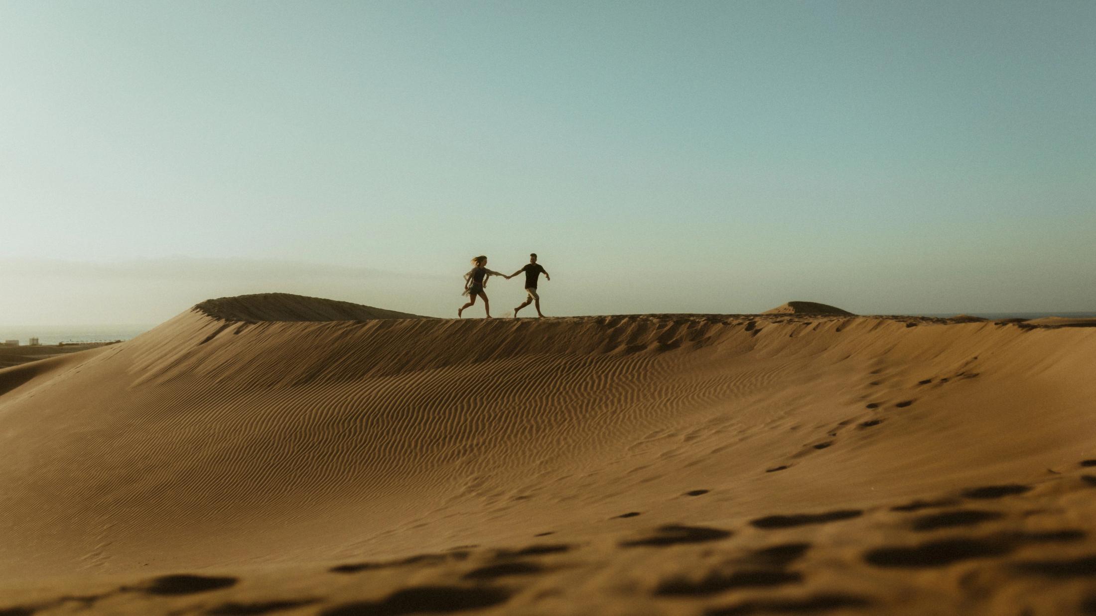 Katja and David running as small silhouettes along a dune ridge.