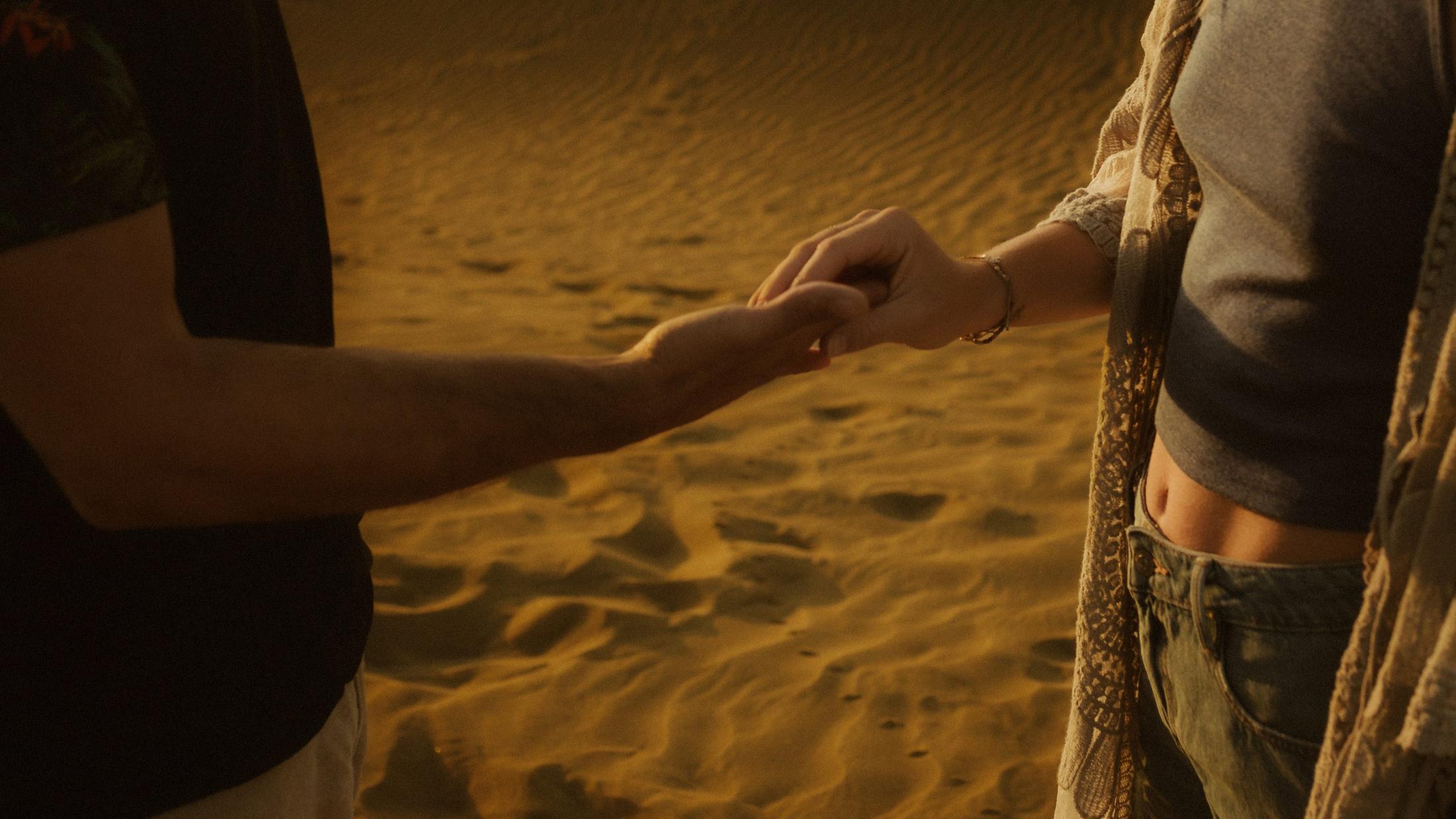 Katja and David touching only their fingertips against the sand.