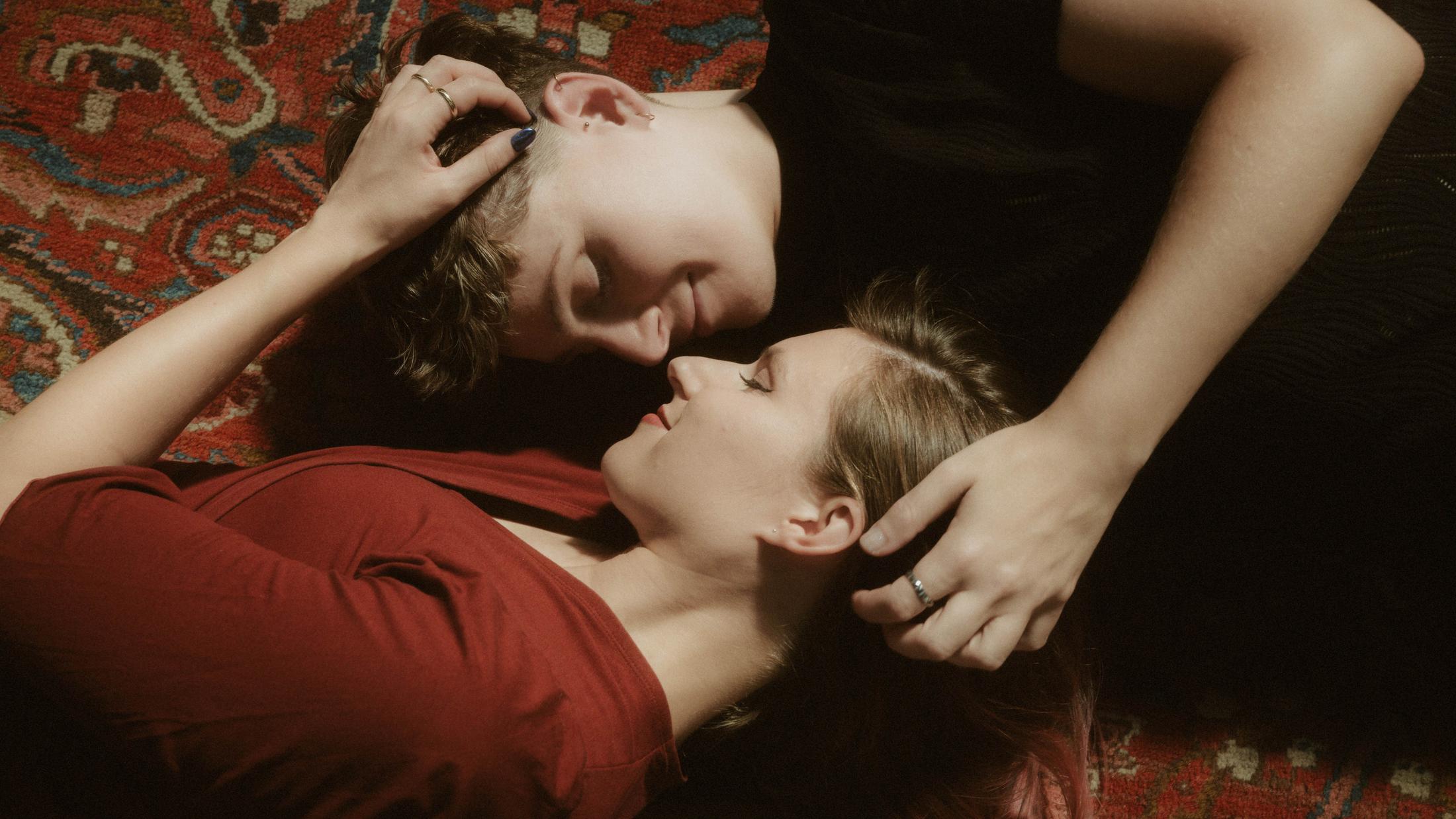 Noah and Michèle lying on the red carpet and looking directly at each other.