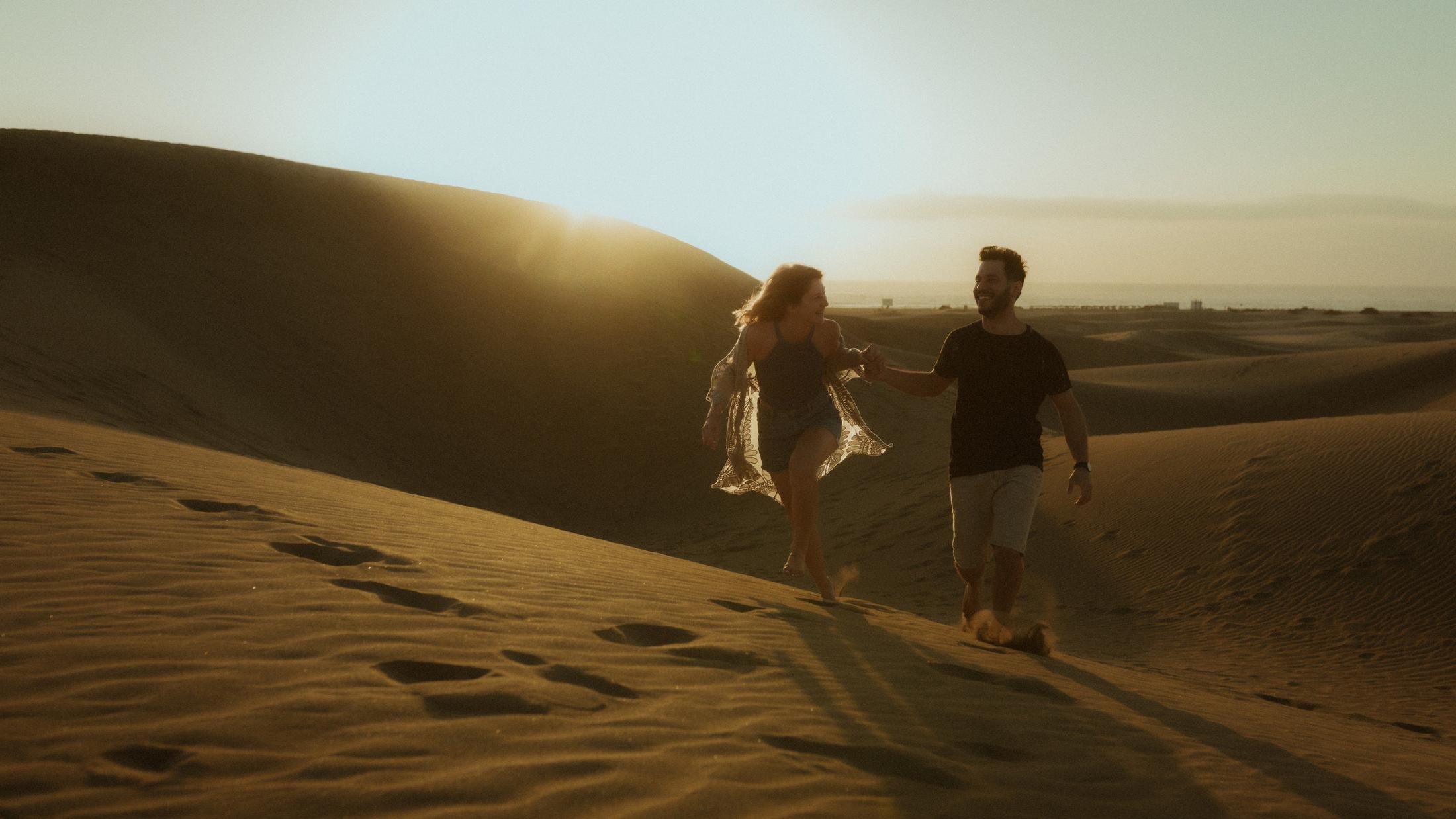 The couple running toward the camera through loose sand.