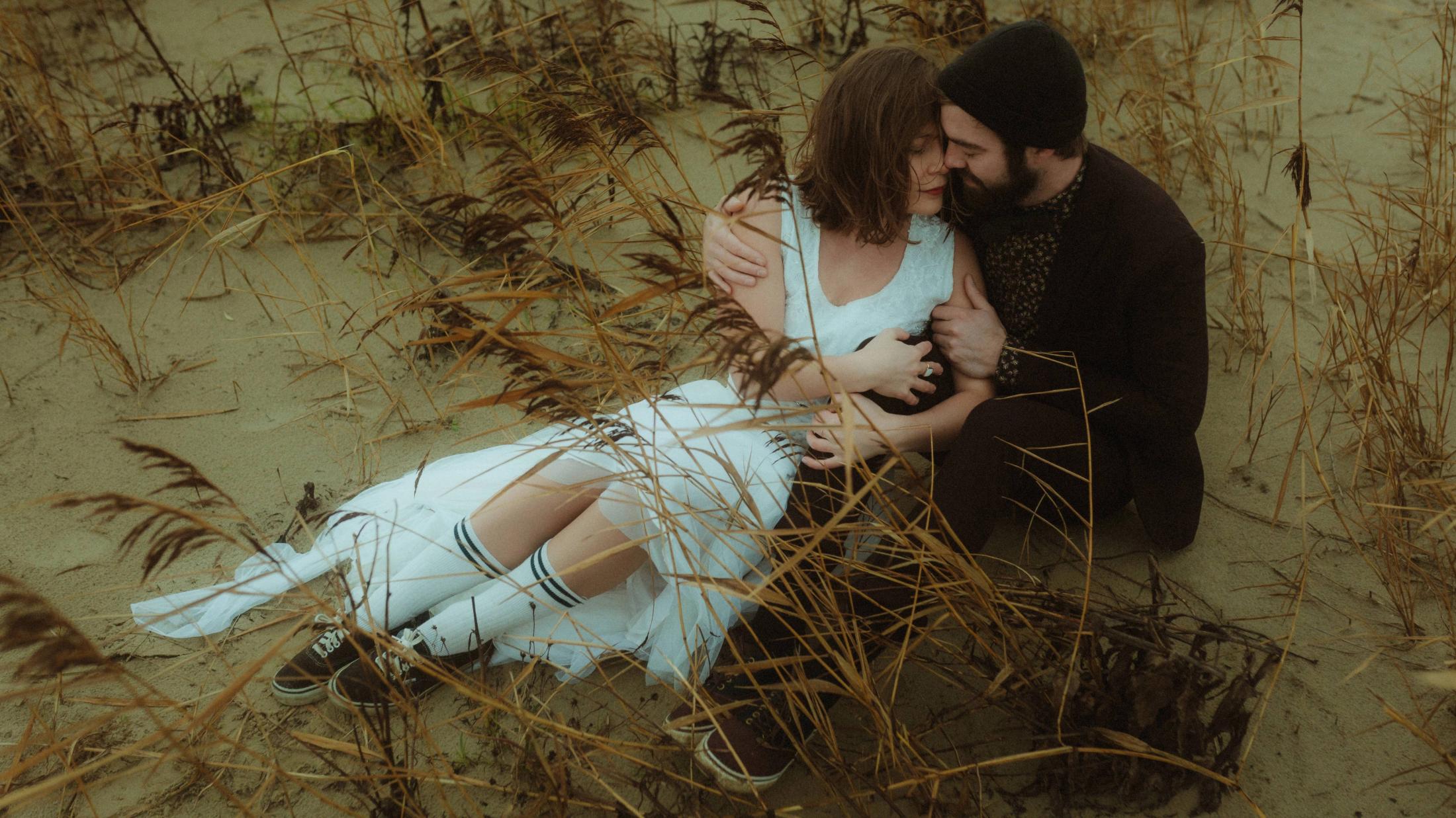 Anni and Daniel sit close together among sand and dry dune grass.