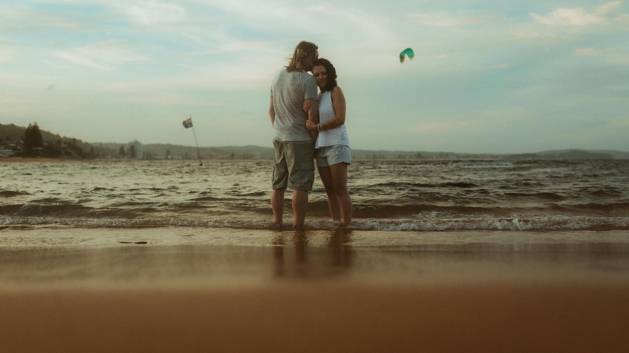 Petra and Roman embracing at the edge of the surf