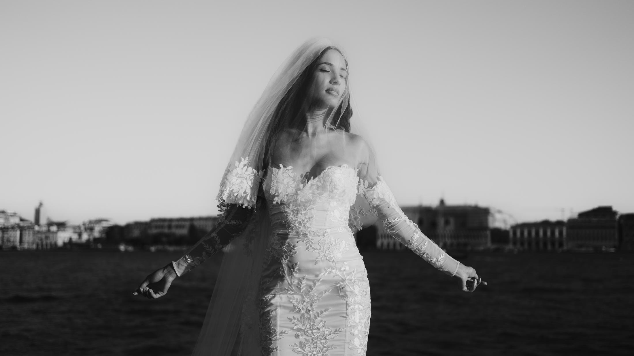 Black-and-white double exposure of the bride moving beside the Venetian lagoon.