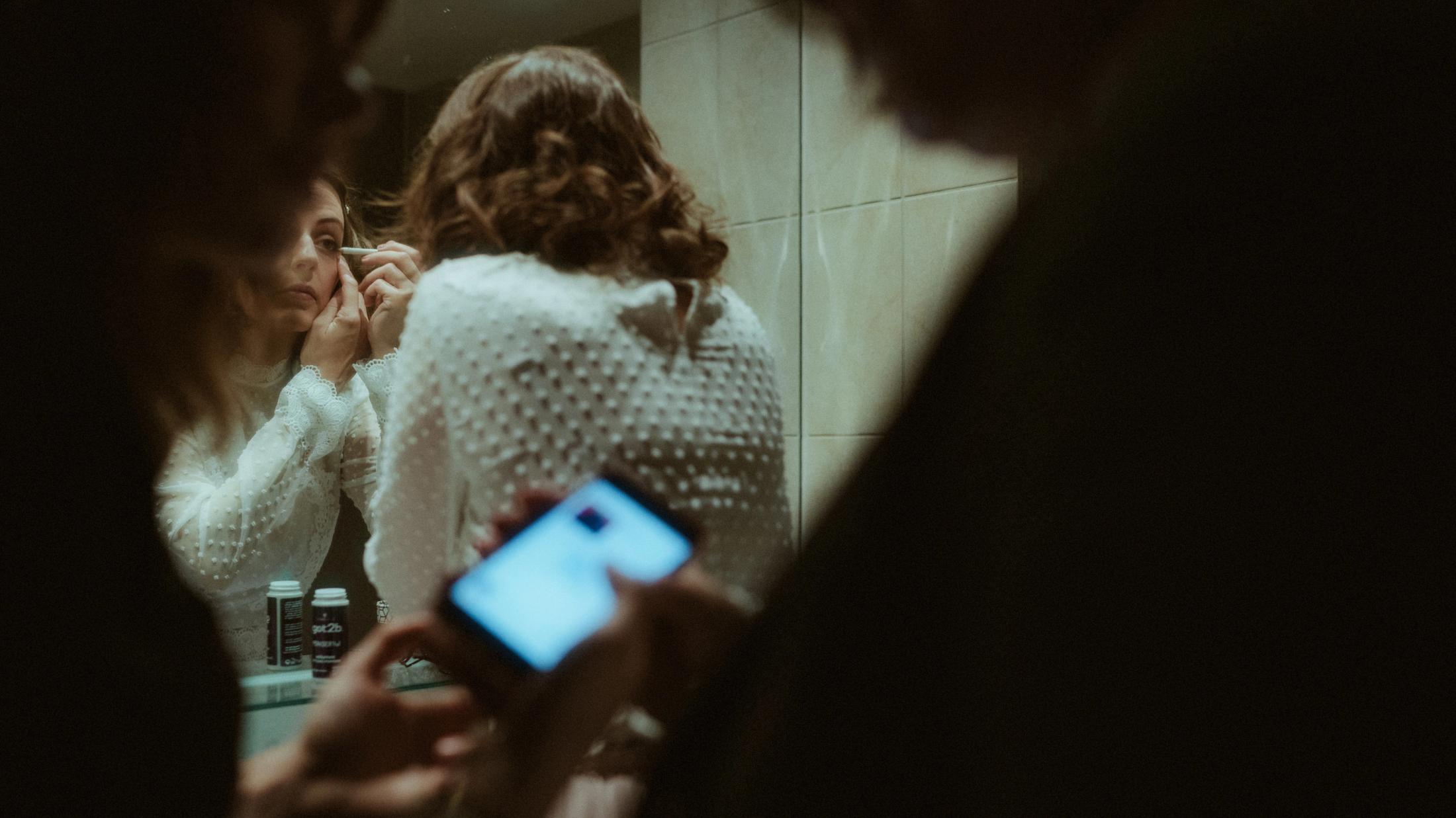 Phone, mirror and several people layered in a small bathroom