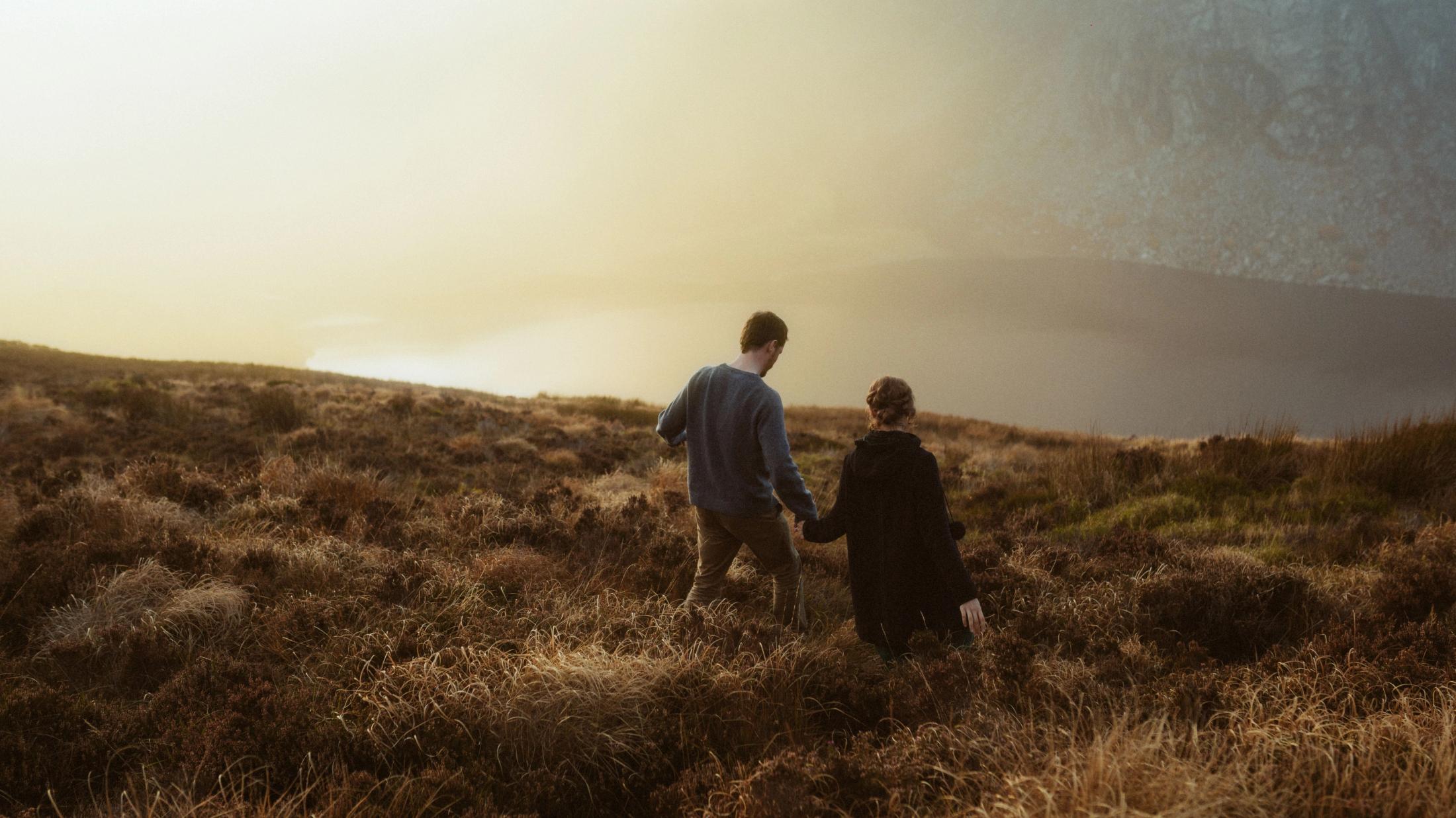 Jule und Rory gehen in Alltagskleidung durch goldenes Moorland, von hinten gesehen.