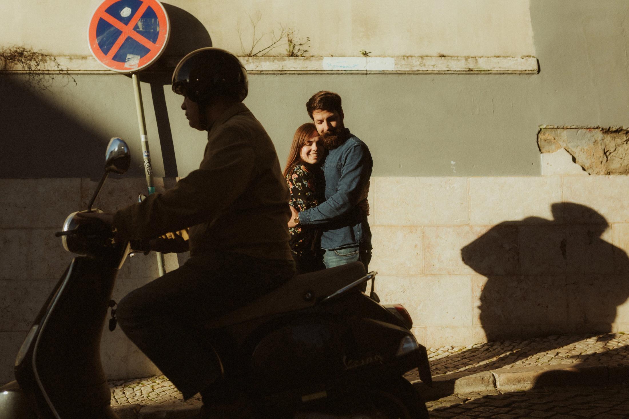 Kathrin and Simon stand in hard evening light behind a passing scooter.