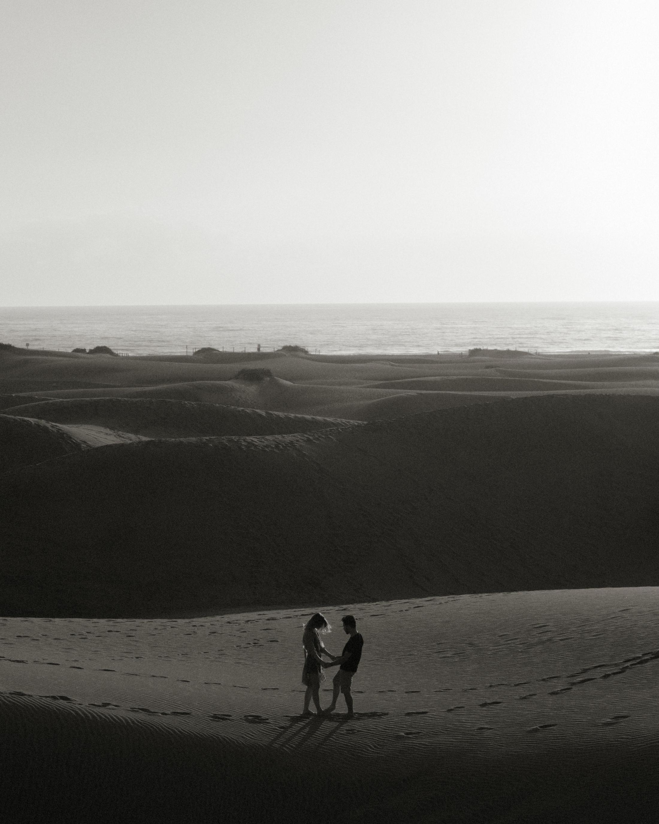 Black-and-white view of Katja and David as tiny figures below the bright sea horizon.