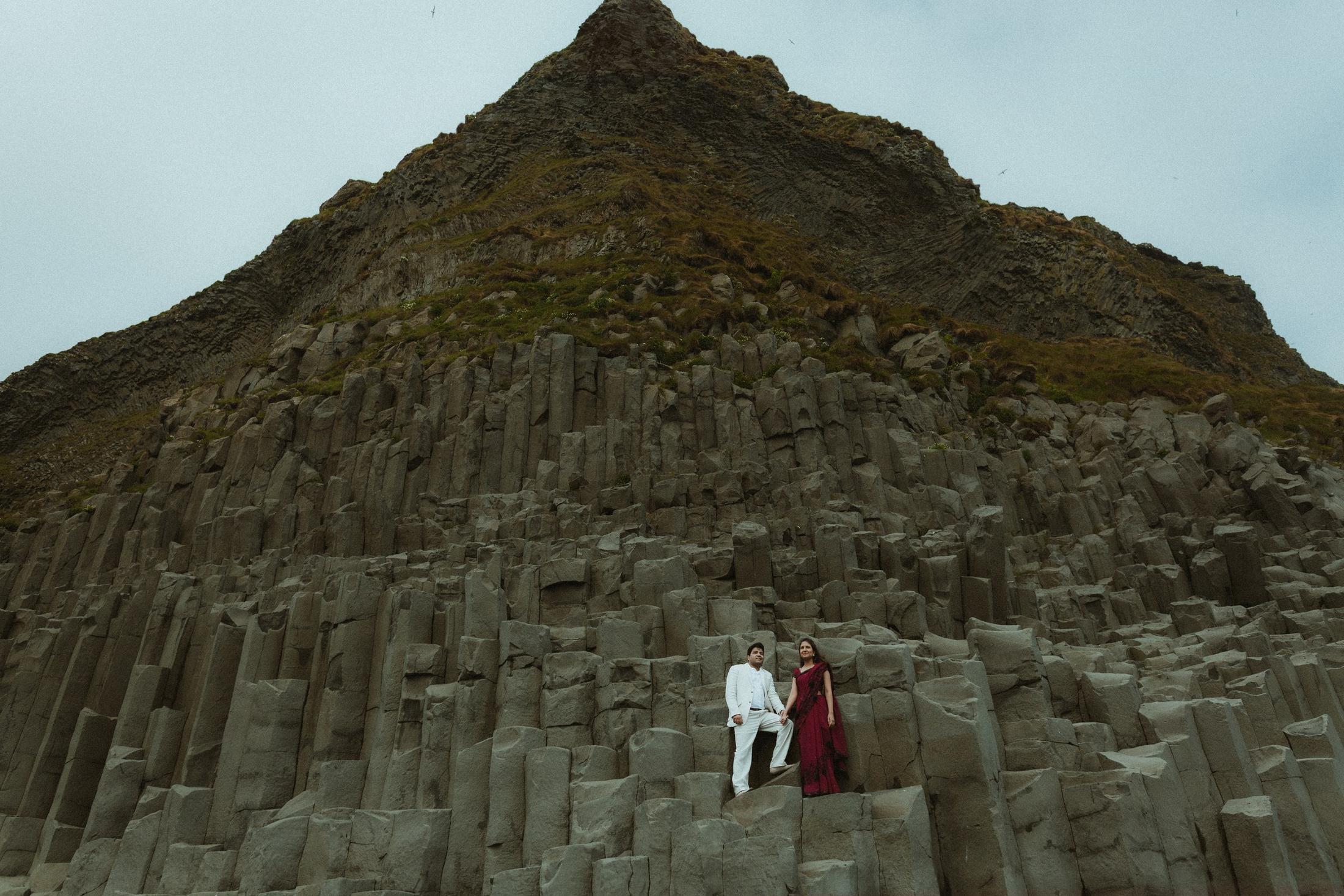 Couple beside tall basalt columns at Reynisfjara.