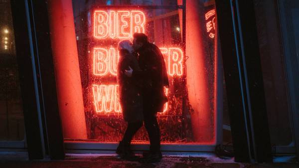 Lorelai and Steffen kiss in falling snow before a red neon window on the Reeperbahn.
