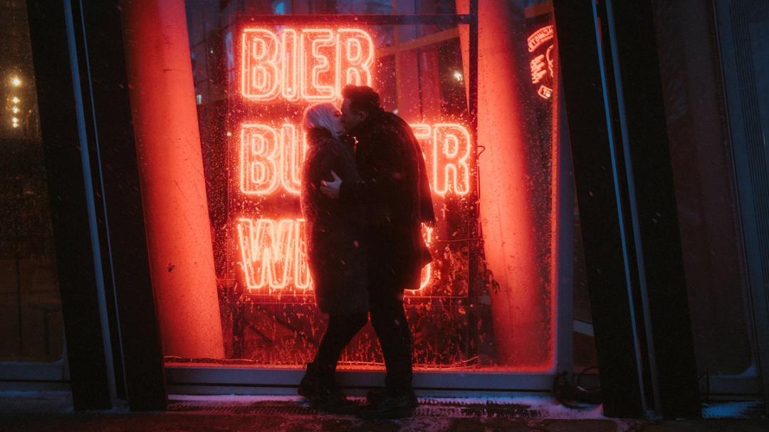 Lorelai und Steffen küssen sich im Schneefall vor einem roten Neonfenster auf der Reeperbahn.