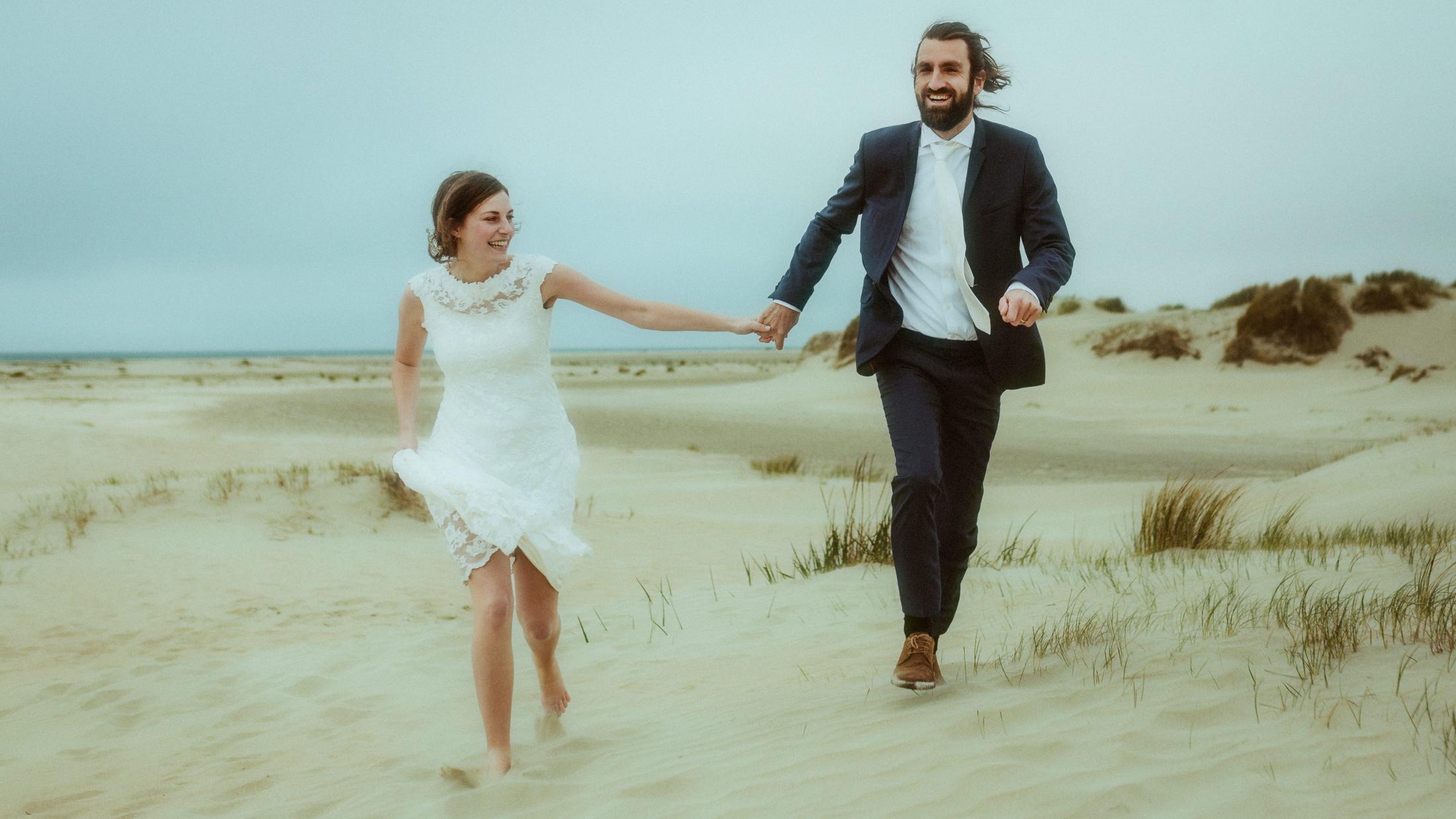 Nina und Torben laufen Hand in Hand und lachend durch die windigen Dünen.