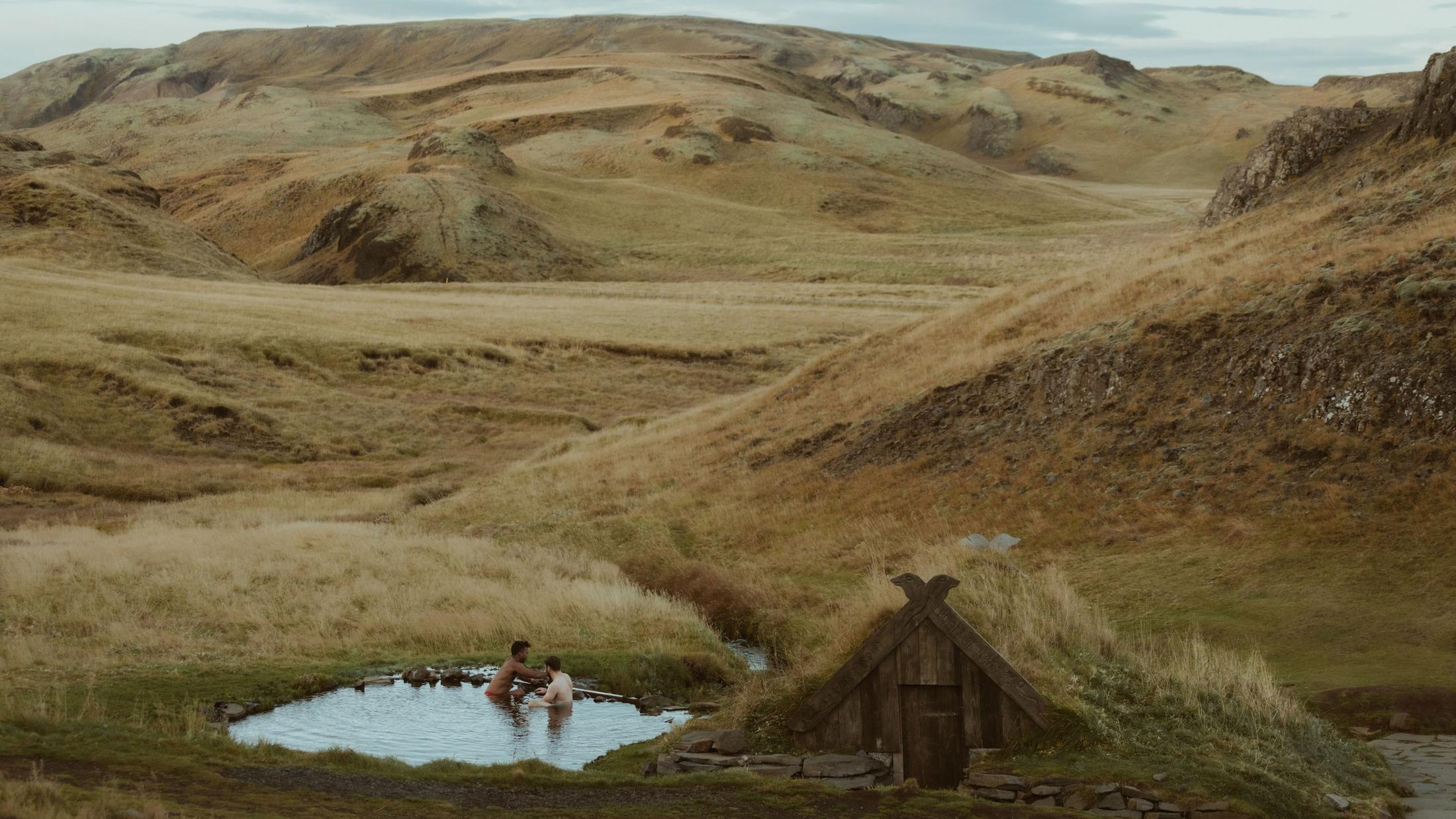 Two people in an outdoor pool surrounded by hills.