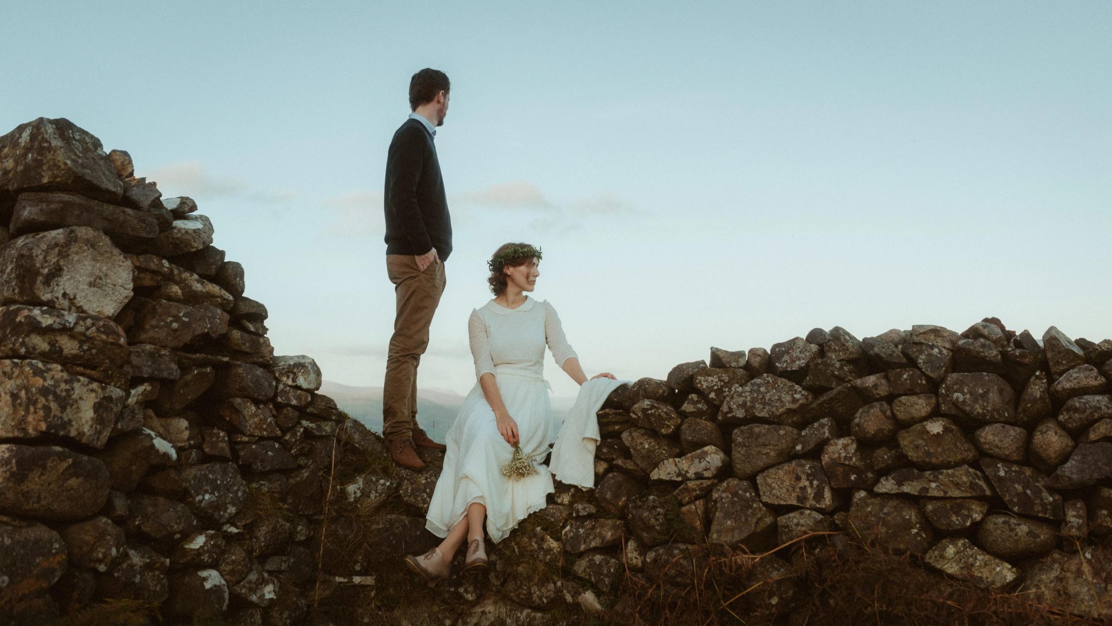 Jule und Rory stehen mit Abstand an einer alten Steinmauer und blicken in verschiedene Richtungen.