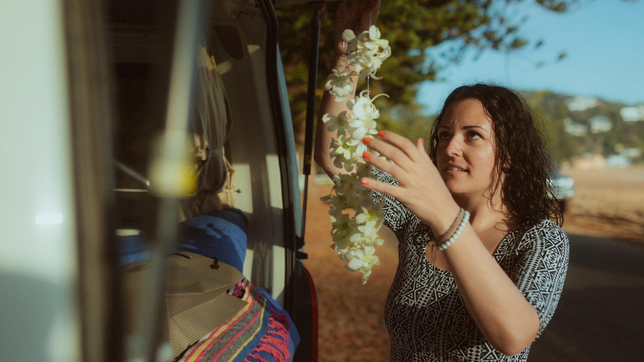 Petra lifting a white flower lei beside the open van