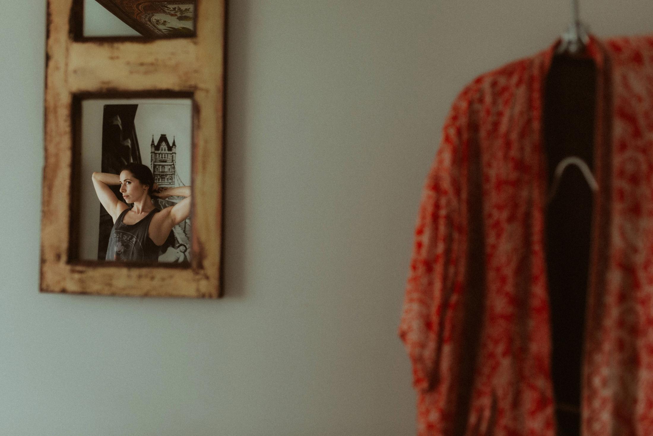 Maya reflected in a small wall mirror beside red fabric.