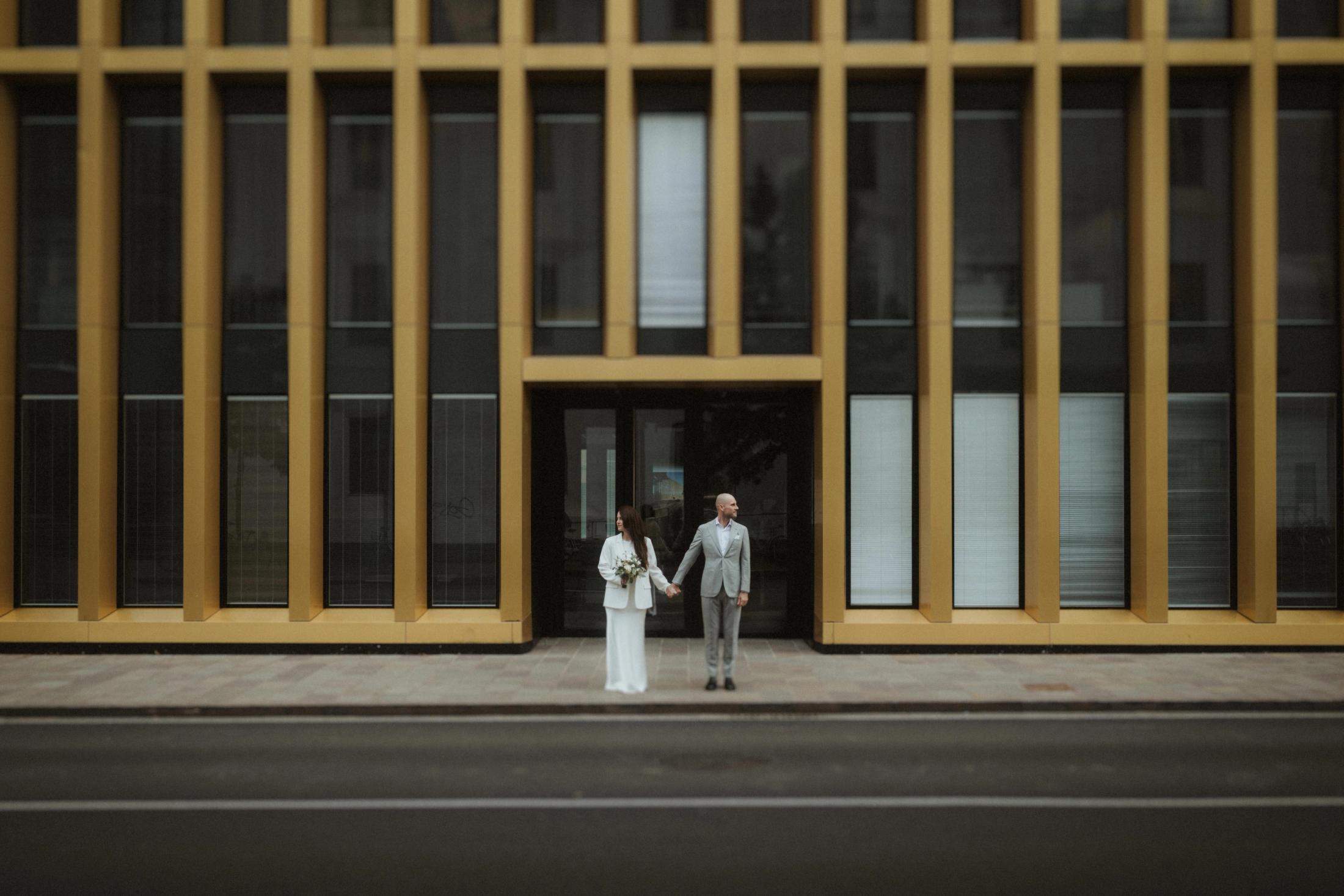 Jana and Steffen standing against a reflective gold-coloured facade.