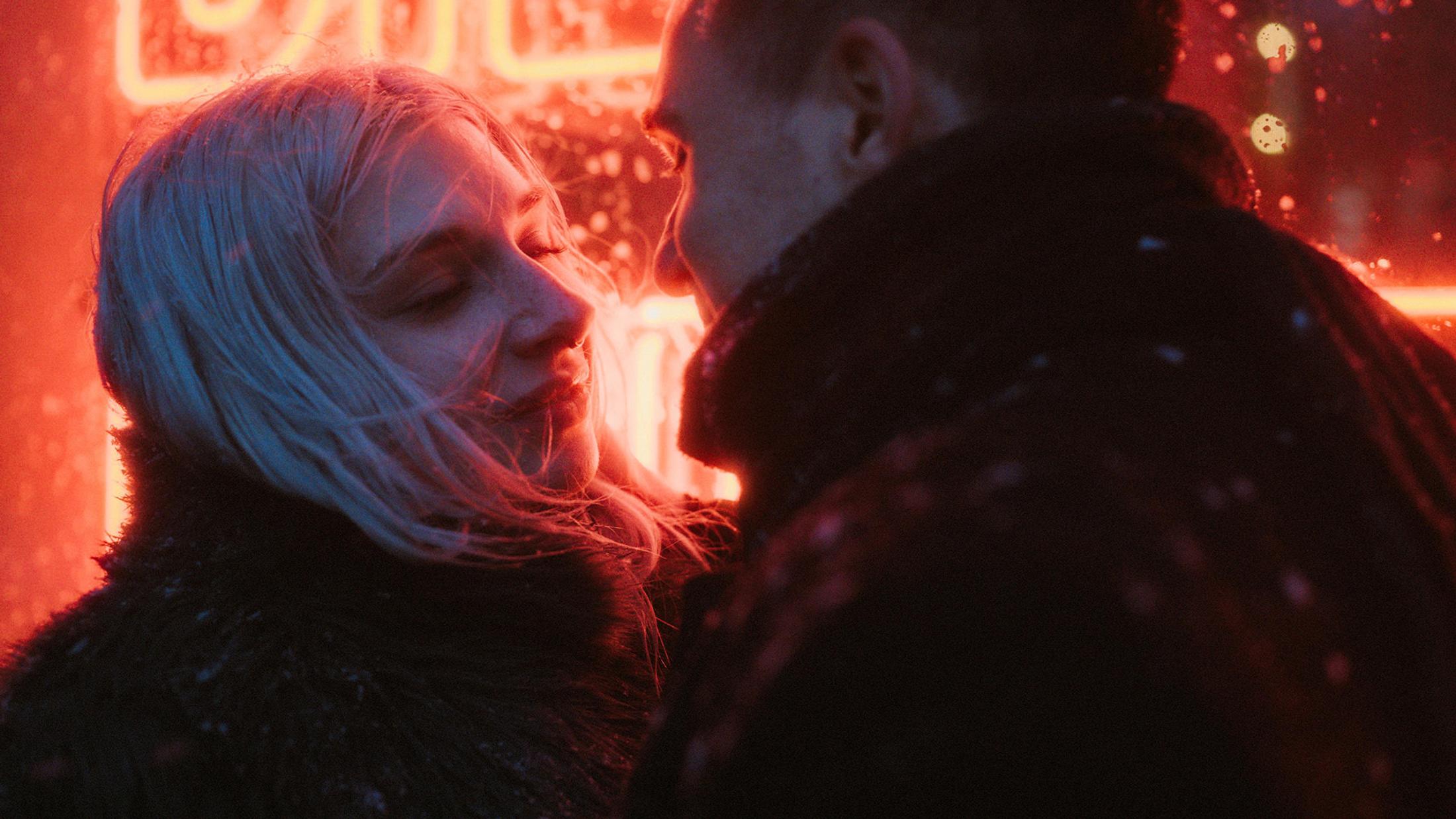 Lorelai and Steffen lean close together in red neon light and falling snow.