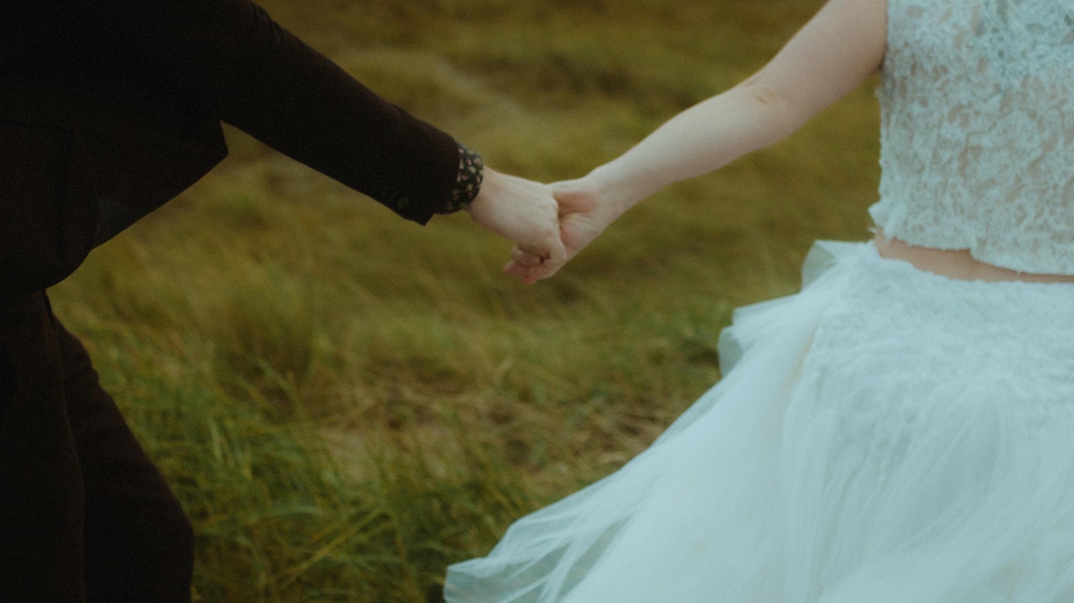 Close view of Anni and Daniel holding hands beside her white dress.