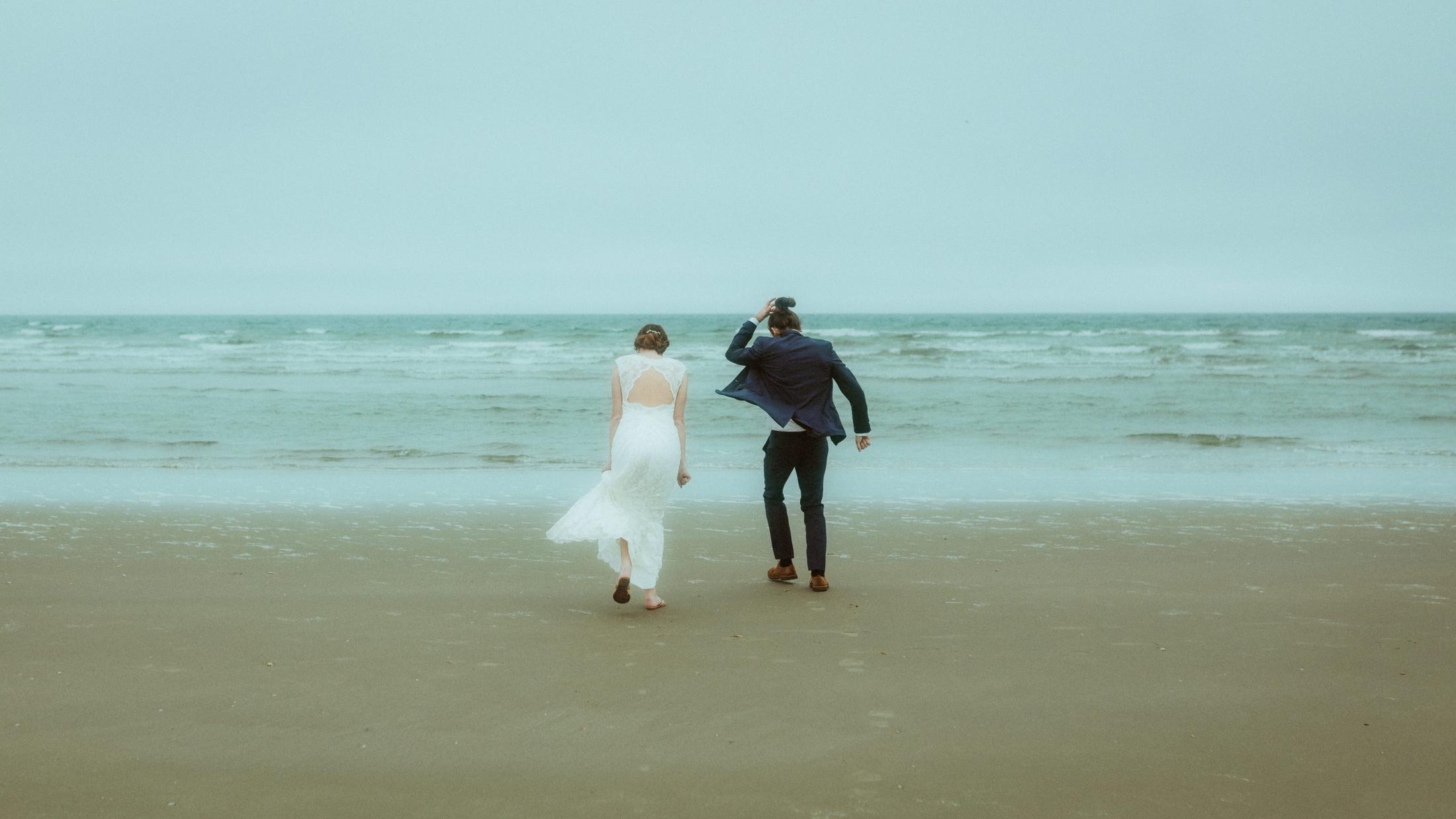Nina und Torben gehen nebeneinander über nassen Sand auf die graue Nordsee zu.