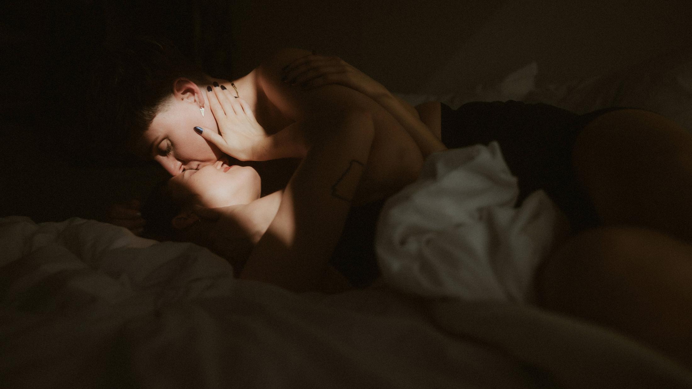 Michèle leaning over Noah as angled window light shapes their faces and bodies.